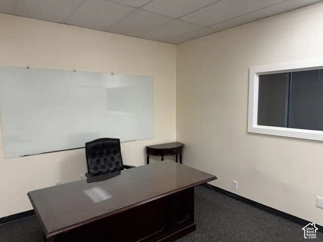 Neutral wall paint, inset glass wall panel, wall-mounted dry-erase board, drop ceiling, and dark carpeting