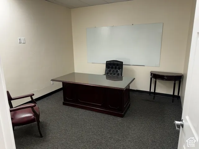 Enclosed room featuring neutral wall paint, dark wall-to-wall carpeting, and a wall-mounted whiteboard