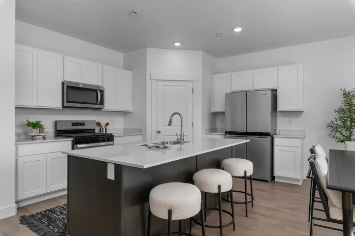 White shaker cabinetry, stainless steel appliances, central island with seating, light-toned countertops, and wood-finish flooring