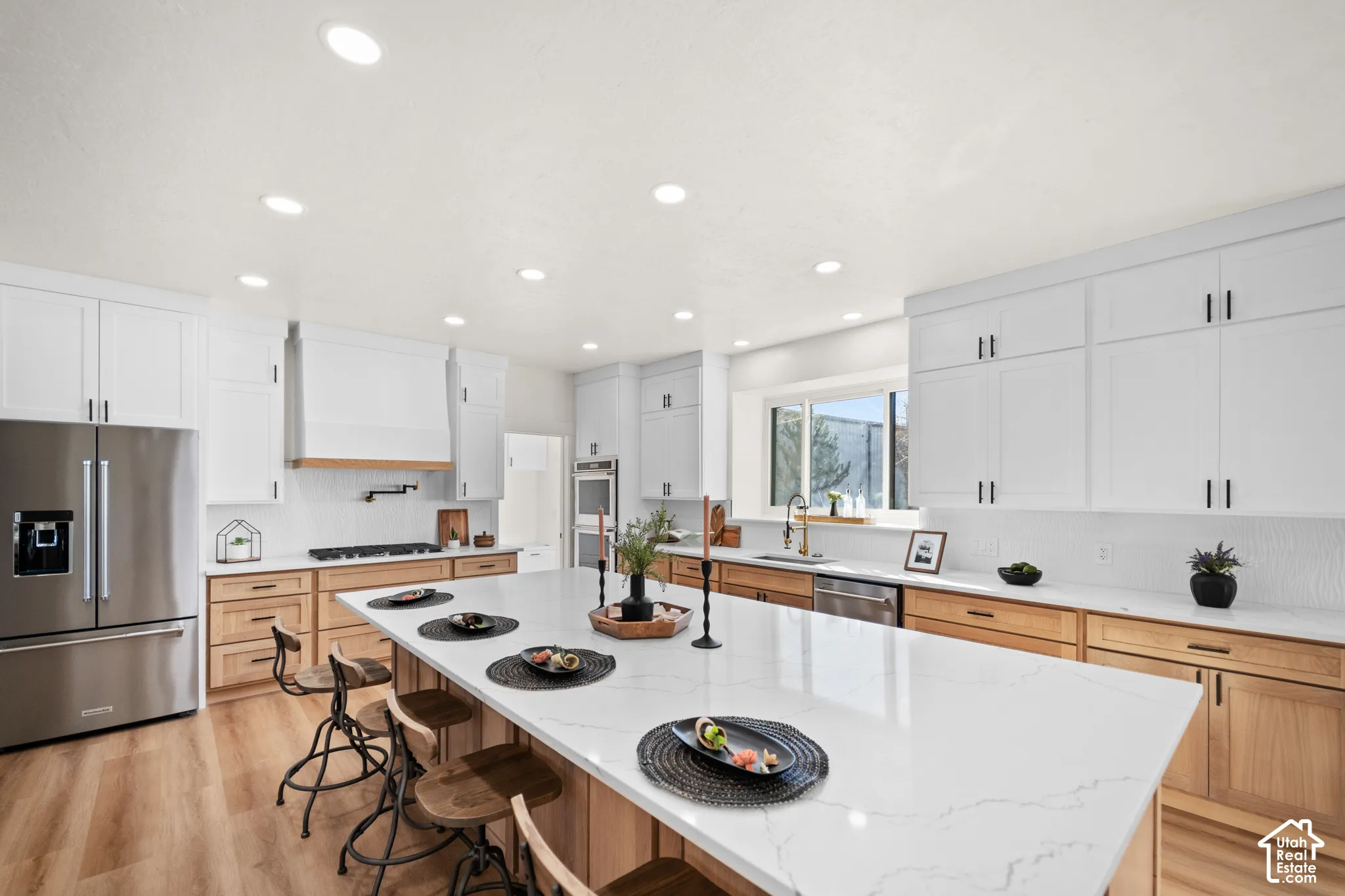 Spacious kitchen featuring an expansive island with seating, stainless steel appliances, wood-finish flooring, white upper cabinetry, and wood-tone lower cabinetry