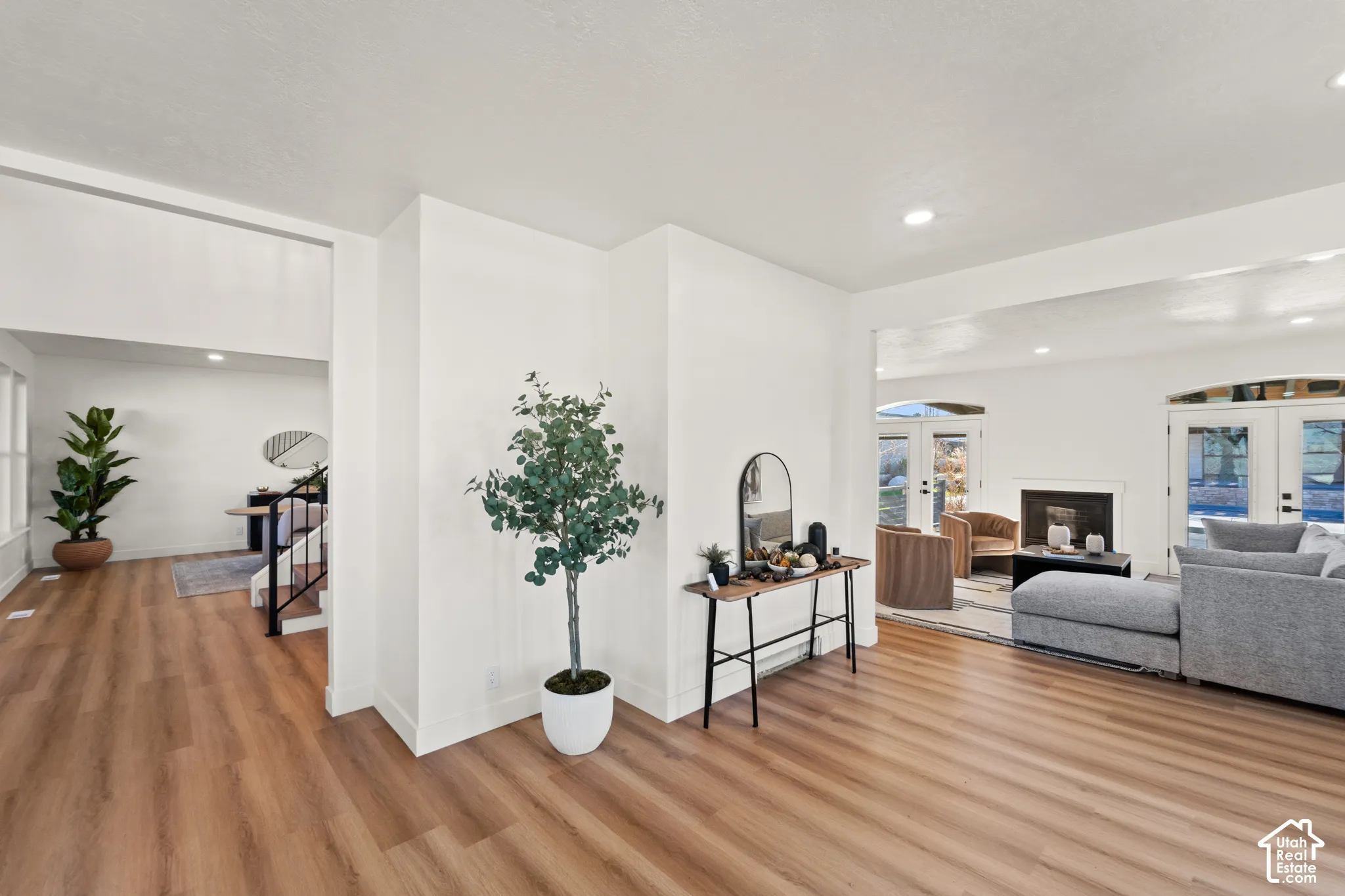 Wood-finish flooring throughout, white walls, recessed ceiling lighting, and a fireplace with a white mantel