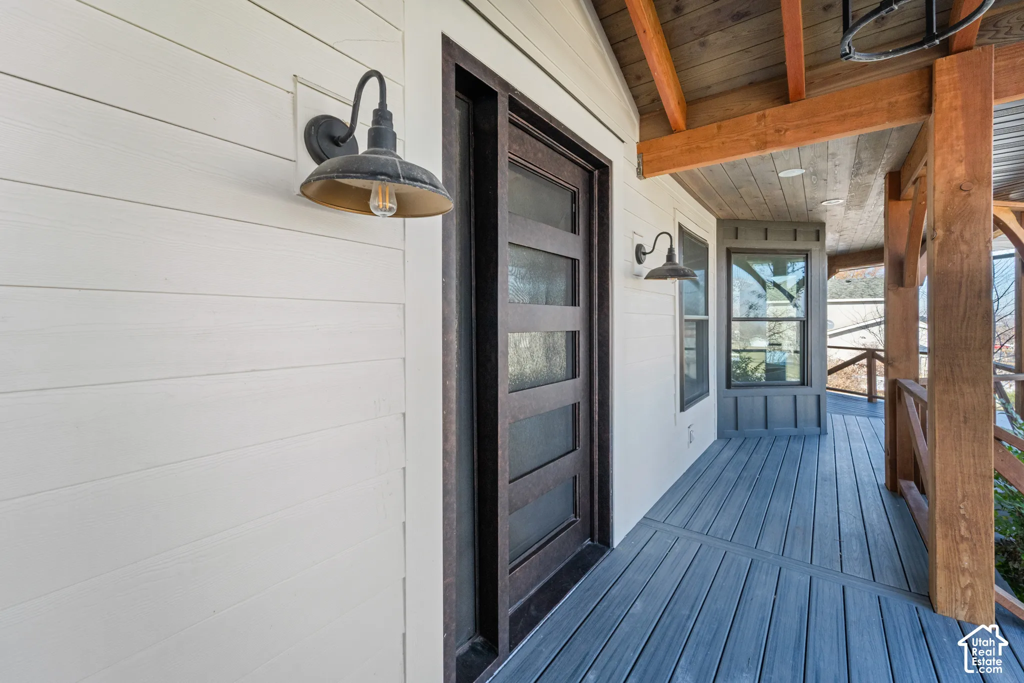 Covered porch with composite decking, industrial-style pendant lighting, and black-framed glass door entry