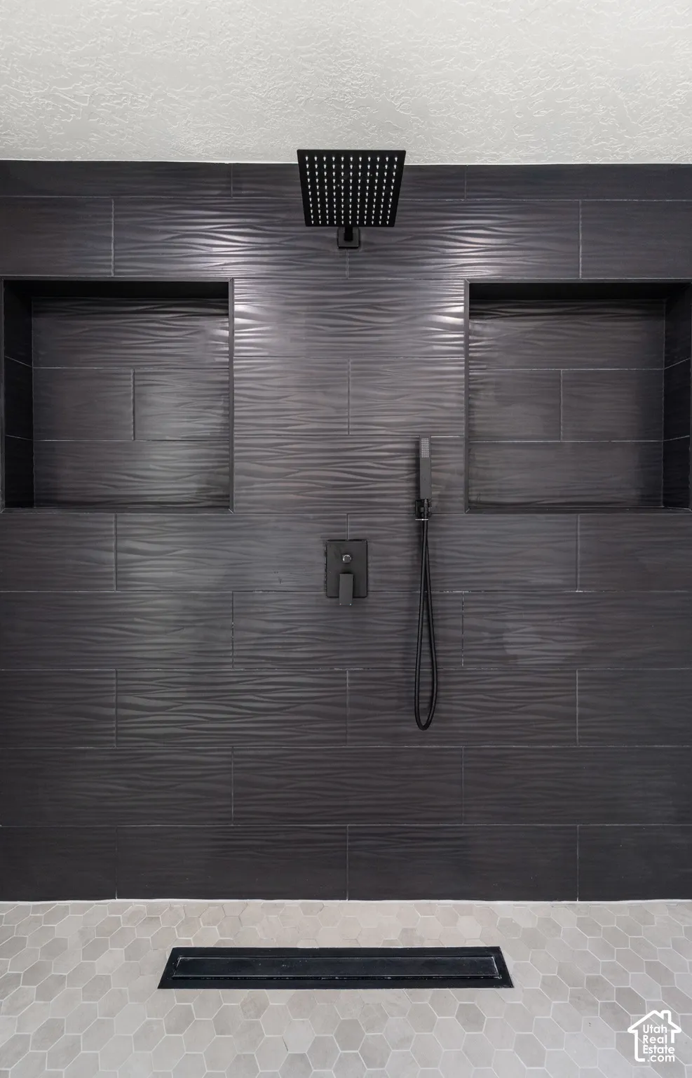 Textured dark gray tile shower surround with two recessed niches, a matte black rainfall shower head, and a linear drain