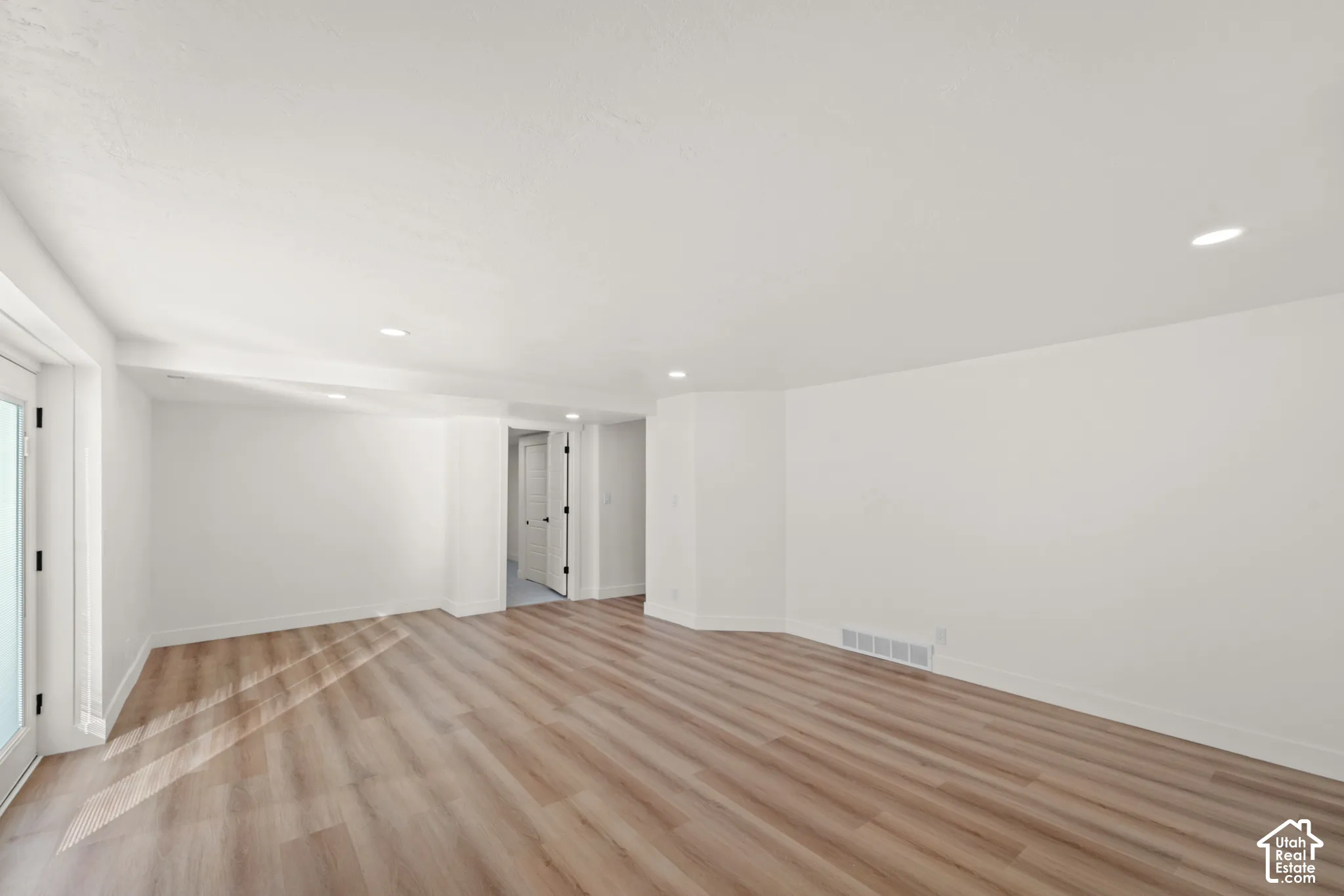 Spacious room featuring wood-finish flooring, recessed lighting, and a white color palette