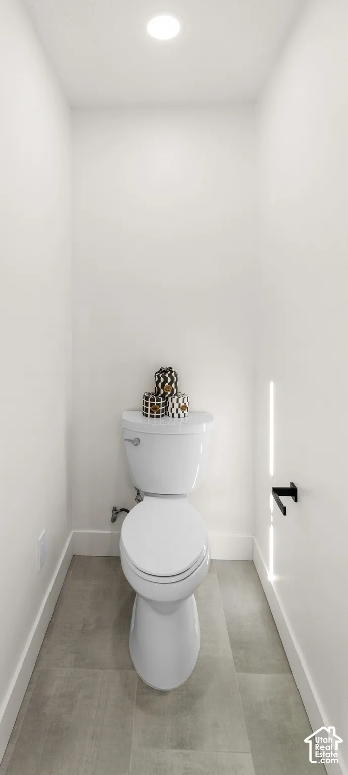 Recessed lighting, white toilet, matte black toilet paper holder, light gray floor tiling, and white wall finishes