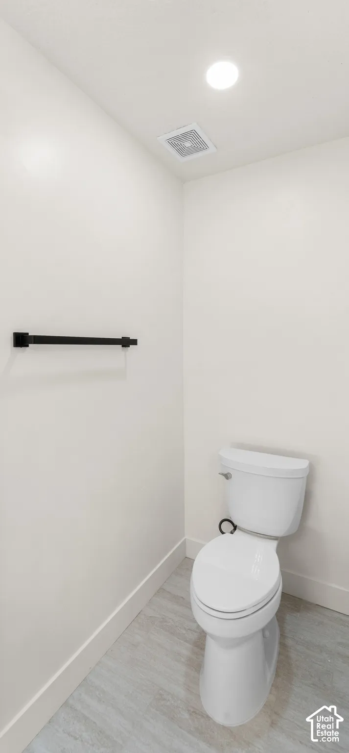 Recessed ceiling lighting, ceiling-mounted exhaust fan, white walls, black towel bar, and light-toned flooring