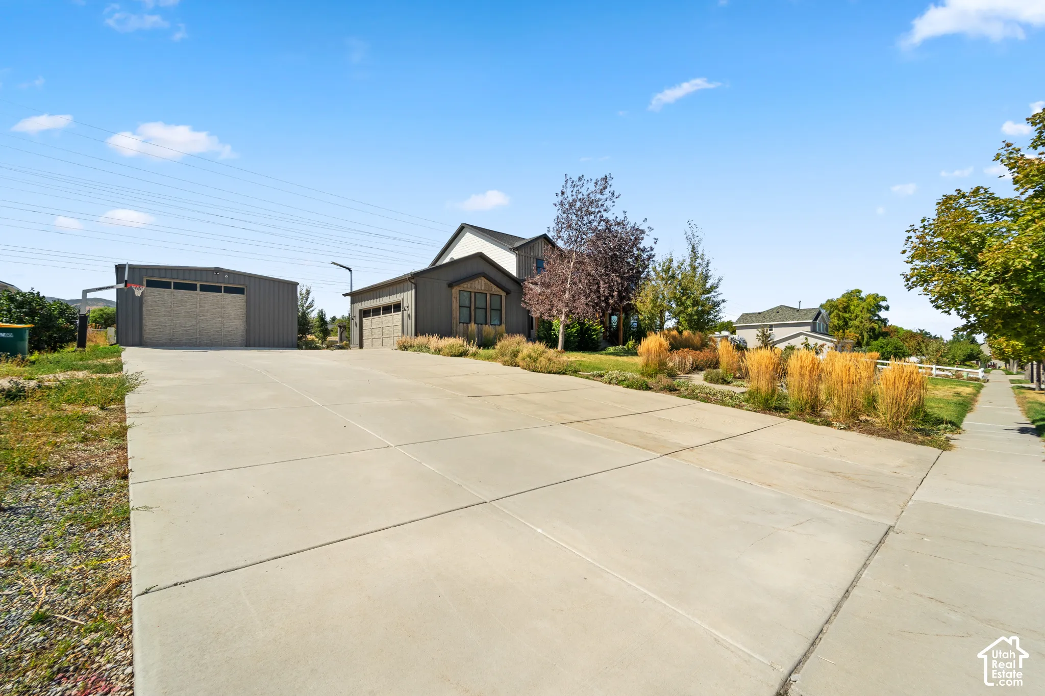 Expansive concrete driveway, detached garage with a basketball hoop, attached garage, and mature landscaping with ornamental grasses