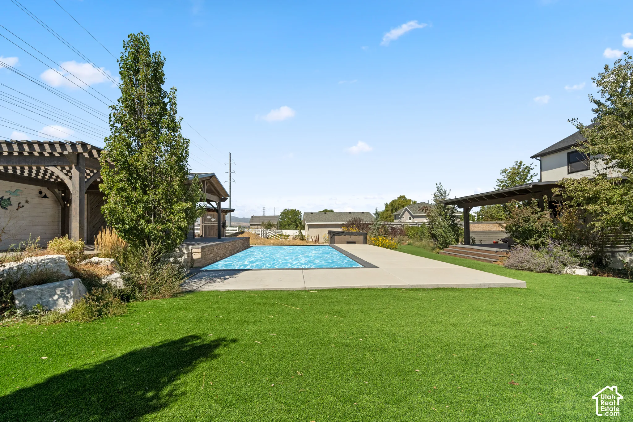 Expansive green space featuring a rectangular swimming pool with surrounding concrete patio