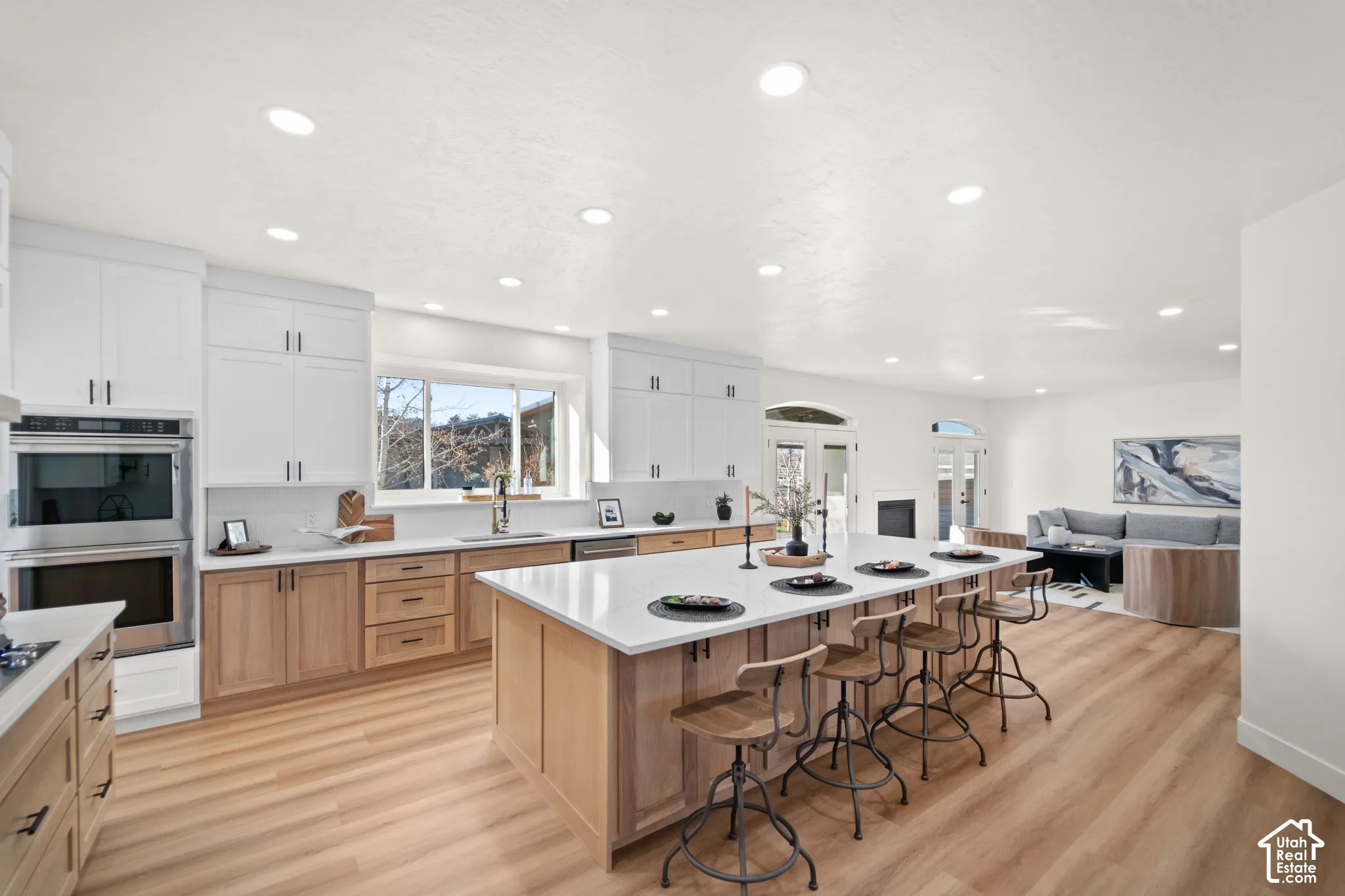Open-concept kitchen featuring an expansive island with seating, stainless steel appliances, two-tone cabinetry, and wood-finish flooring