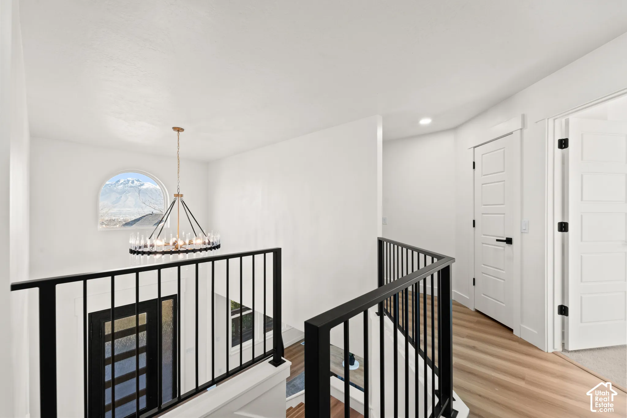 Arched window with mountain scenery, contemporary chandelier, black metal railings, wood-finish flooring, and white paneled doors