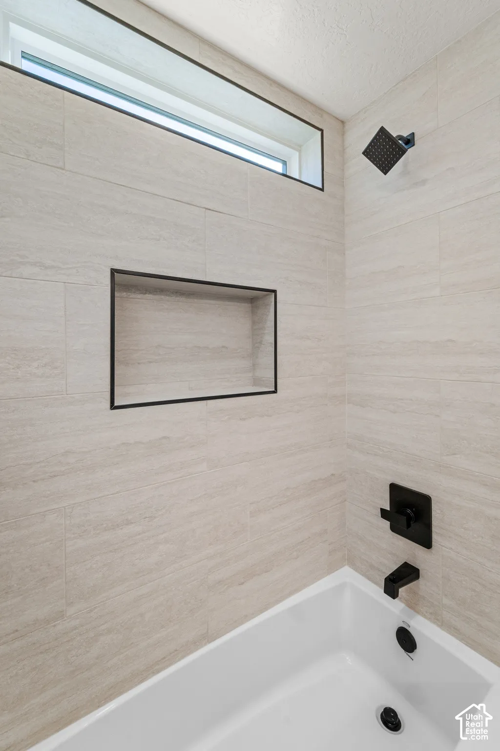 Built-in bathtub with matte black fixtures, full-height tiled surround, recessed wall niche, and transom window