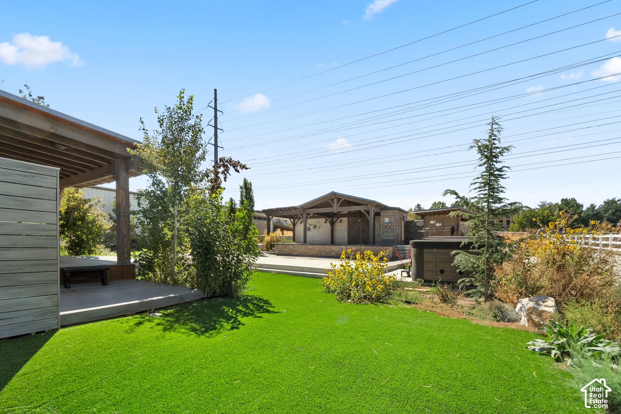Expansive green space featuring artificial turf, a covered patio with wooden beams, a built-in outdoor structure with a stone facade, and mature landscaping