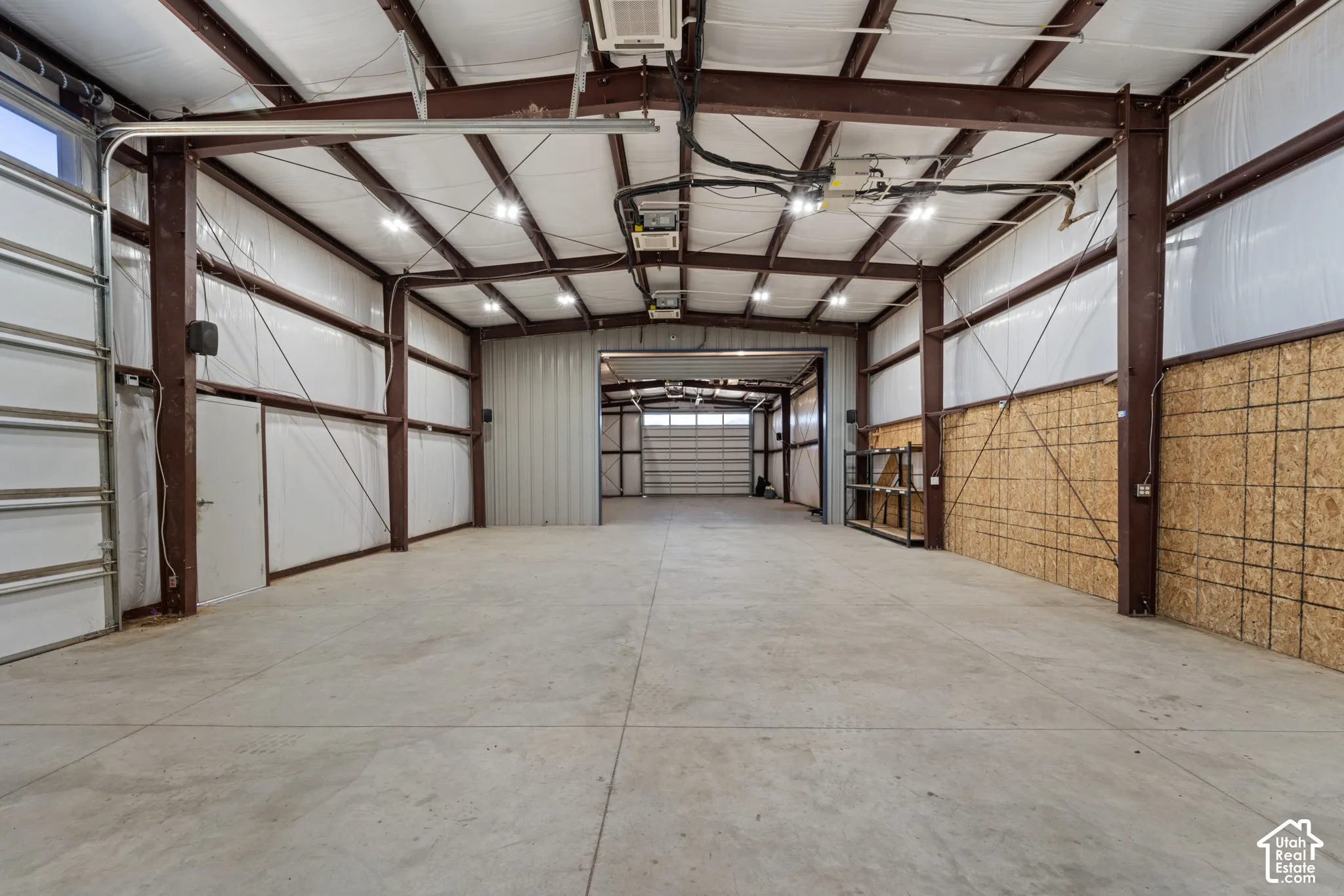 Expansive warehouse space featuring a concrete floor, exposed structural beams, insulated walls, overhead lighting, and multiple roll-up doors