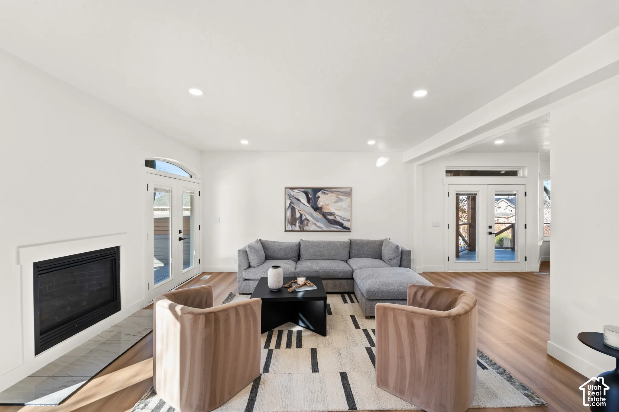 Open-concept living space with wood-finish flooring, a built-in fireplace featuring a tile hearth, recessed lighting, and white walls