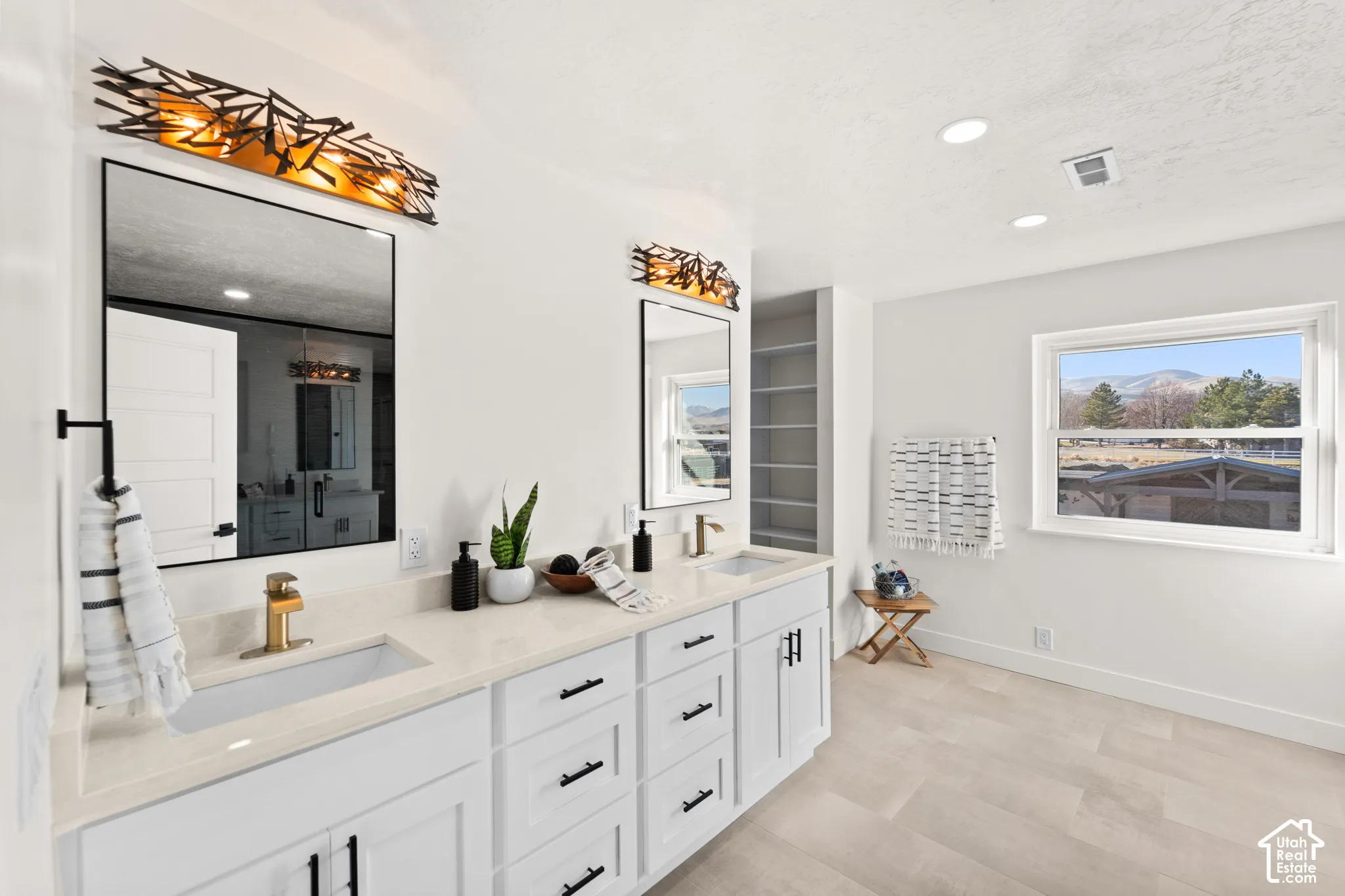 Double vanity with white cabinetry and light-toned countertops, featuring rectangular undermount sinks and modern gold-toned faucets