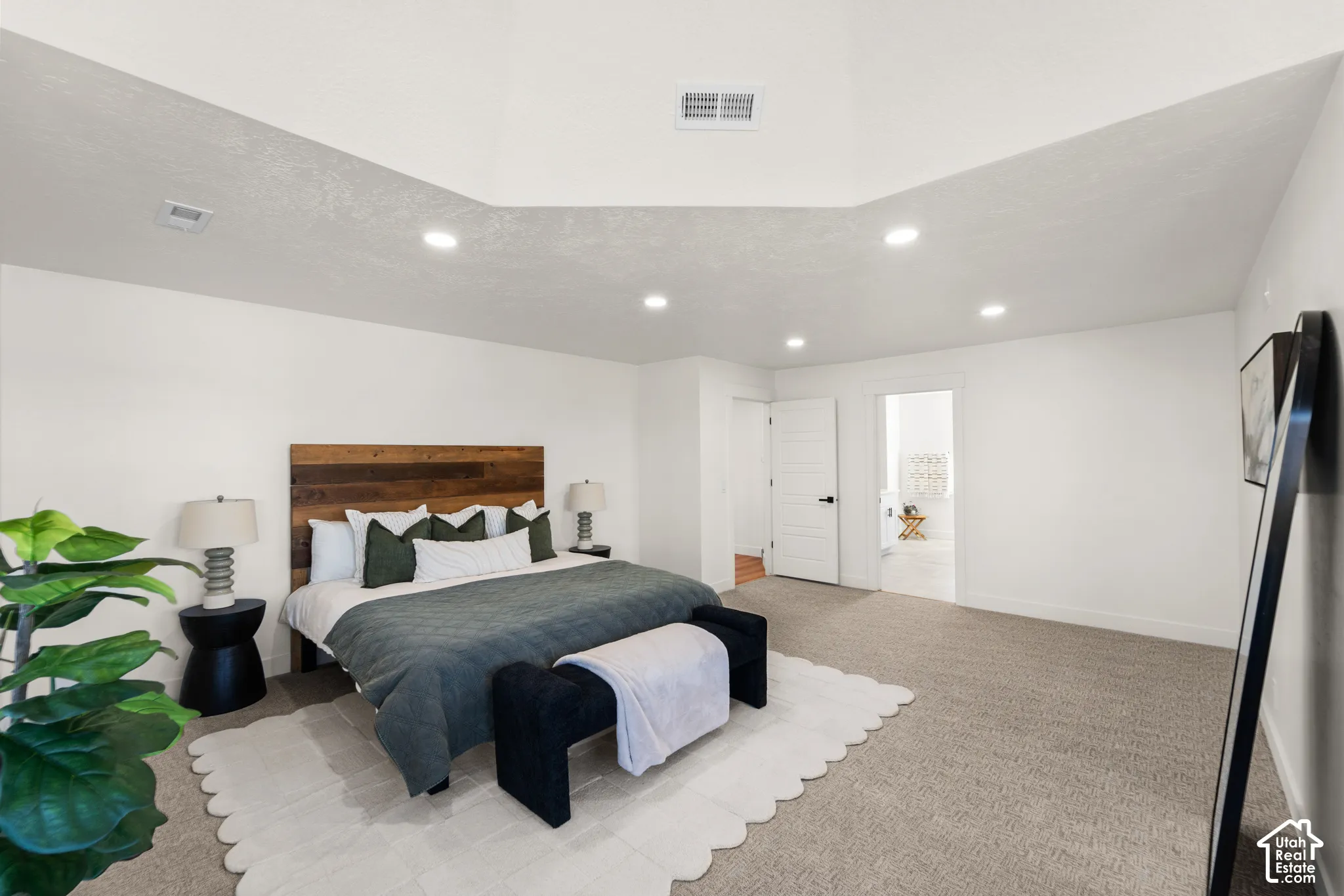 Vaulted ceiling with recessed lighting, wood-finish headboard, and light-toned carpeting