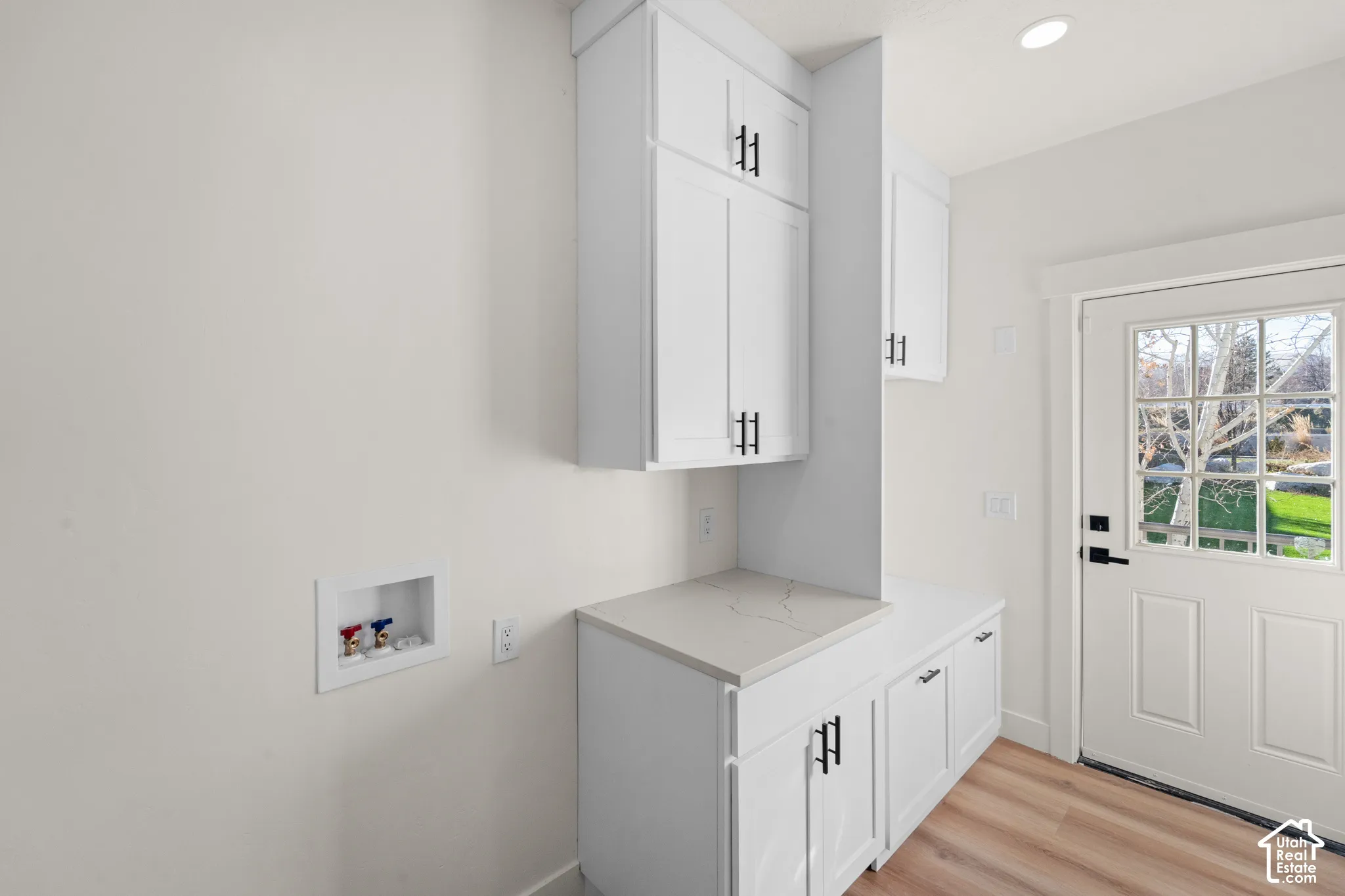 White cabinetry, stone-finish countertop, wood-finish flooring, recessed lighting, and a white paneled door with glass inserts