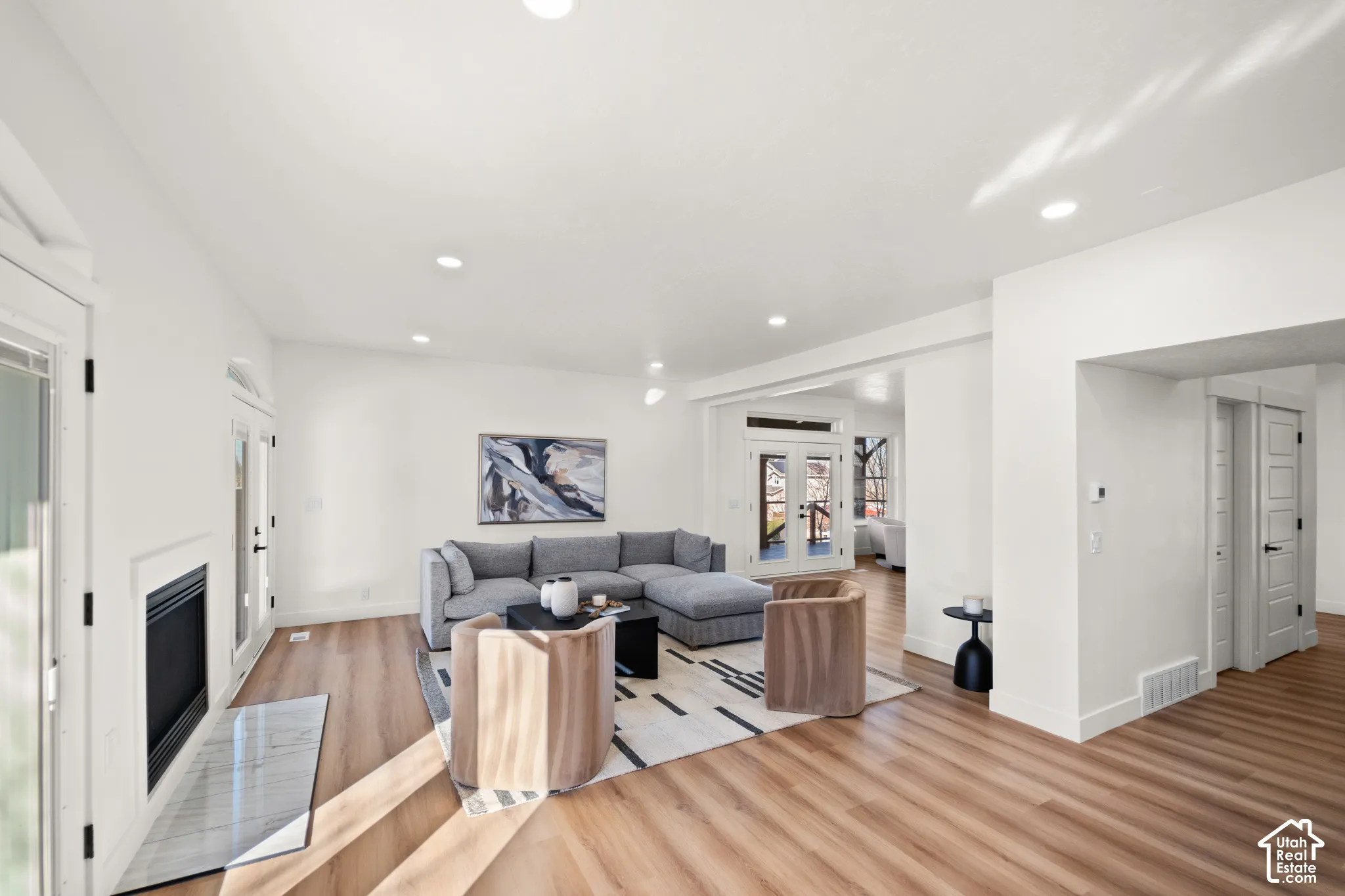Spacious living area featuring wood-finish flooring, recessed lighting, and a fireplace with a stone-finish hearth