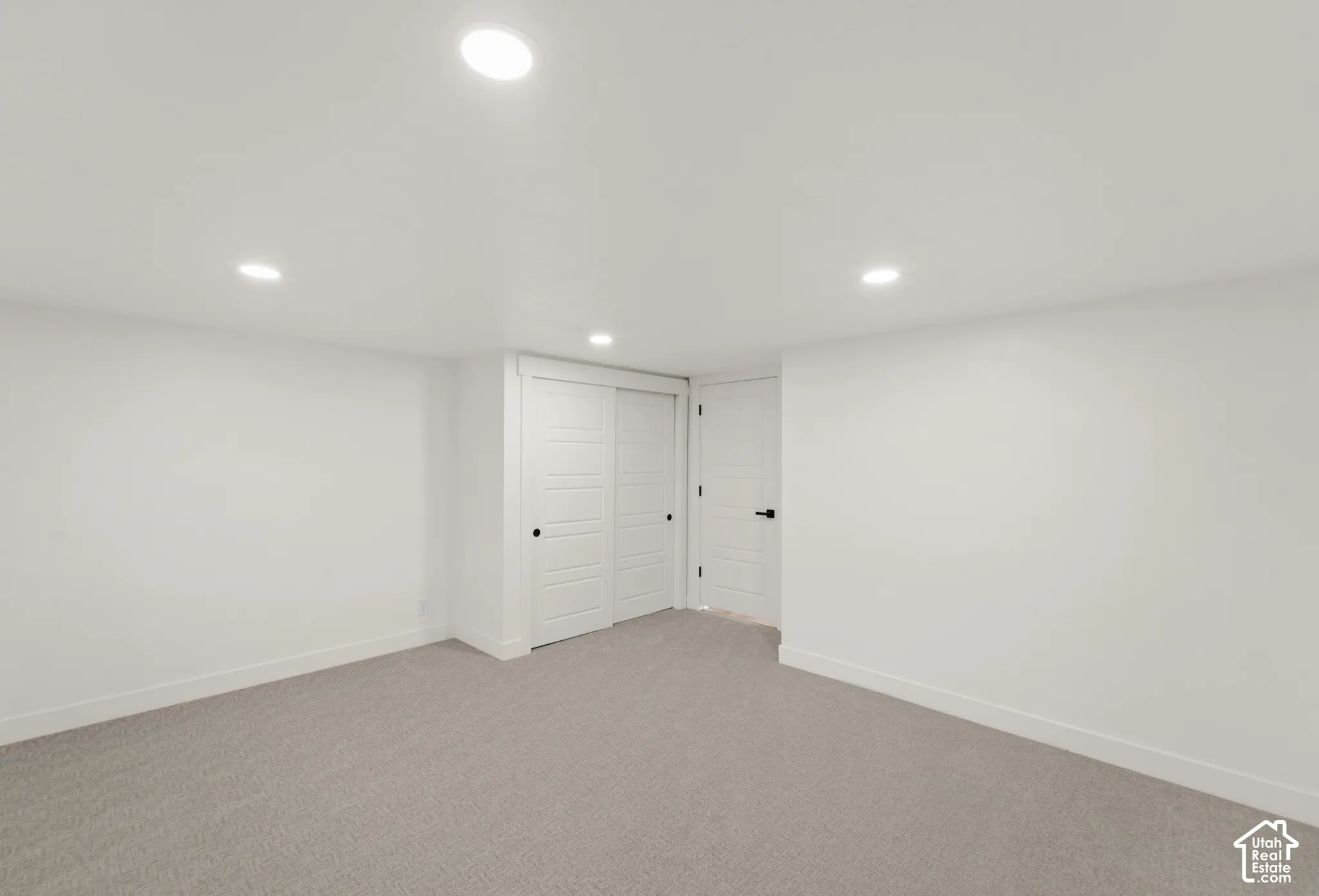 Recessed lighting illuminates neutral-toned carpeting and bright white walls