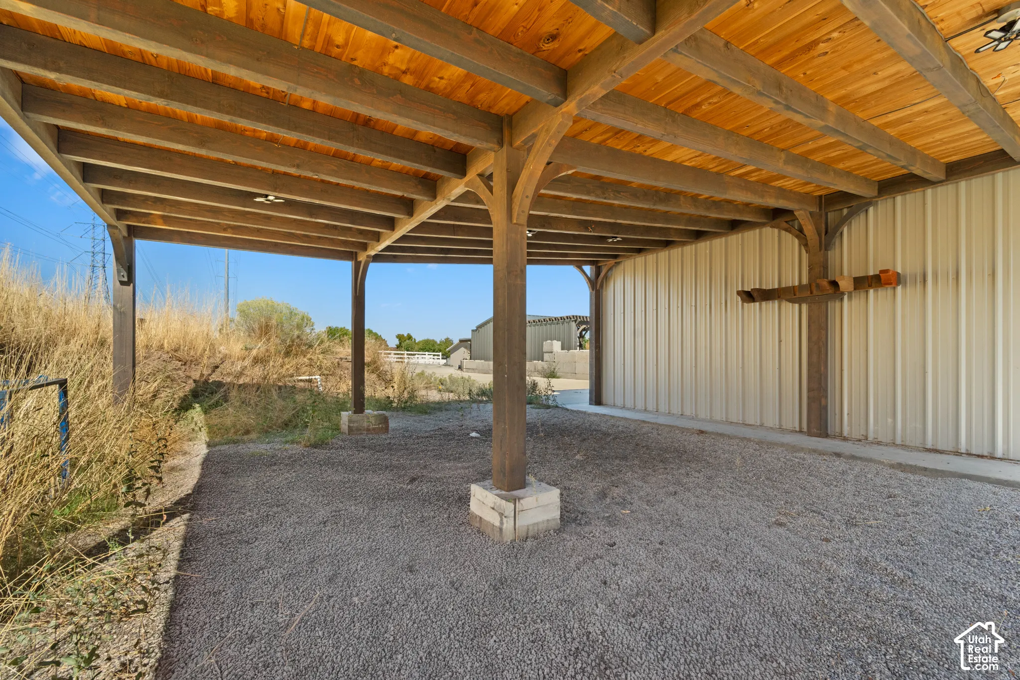Covered outdoor structure with exposed wood beams, finished wood ceiling, and gravel flooring