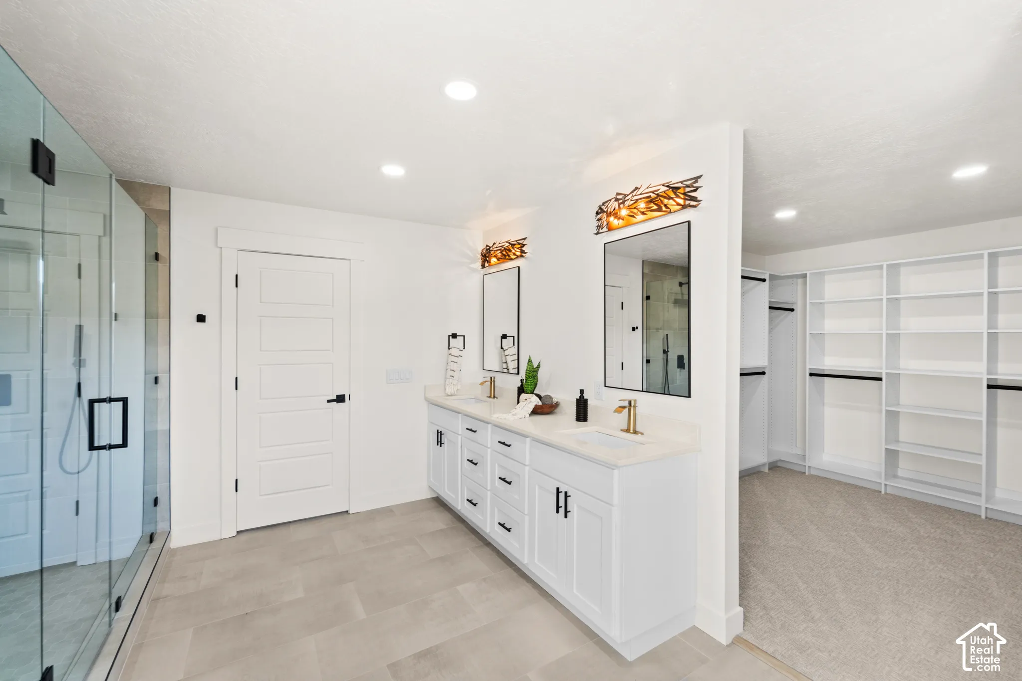 Spacious bathroom featuring a dual vanity with white cabinetry, gold-finish fixtures, and a glass-enclosed shower