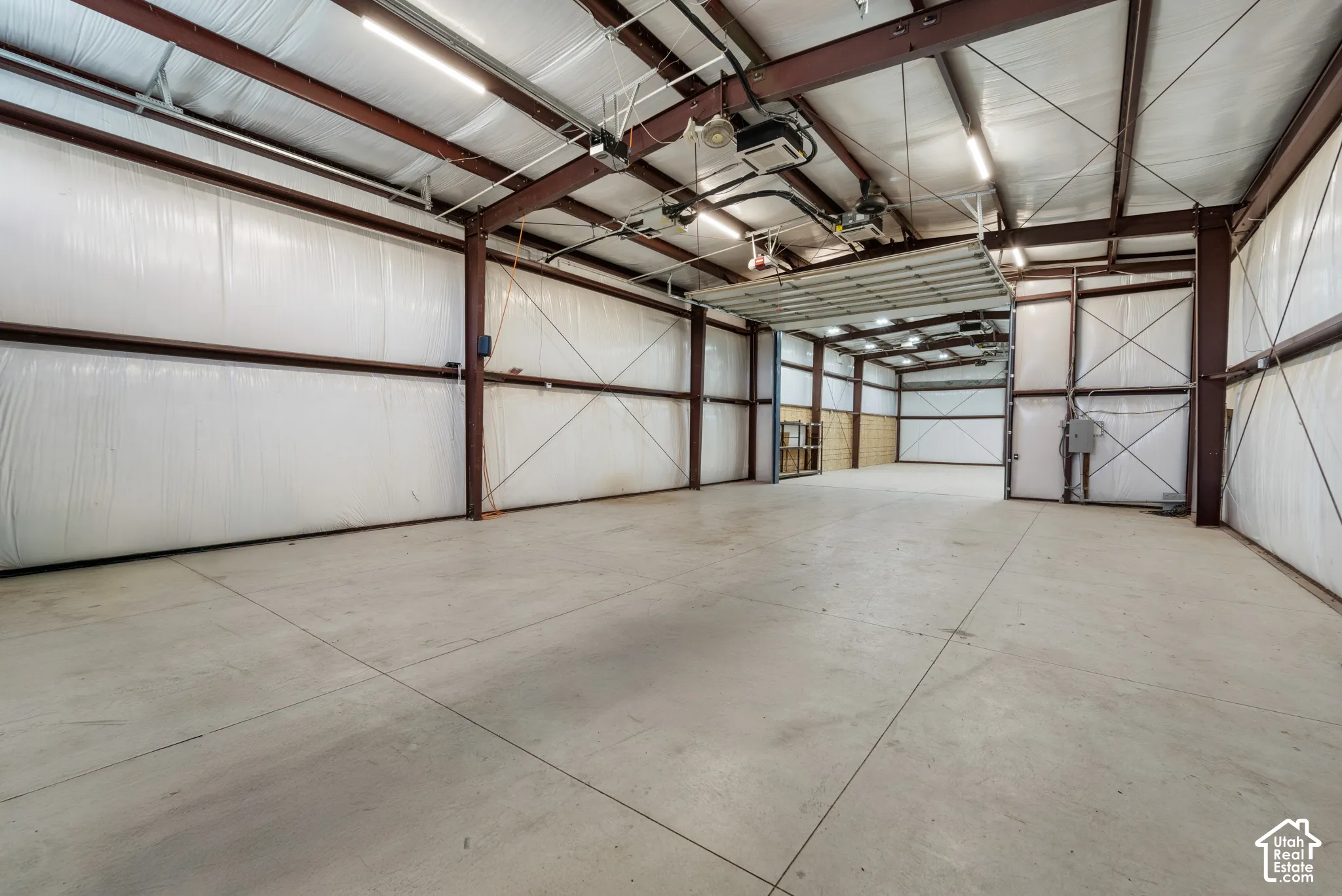 Spacious concrete flooring with exposed structural beams, high ceilings, bright overhead lighting, and an overhead door