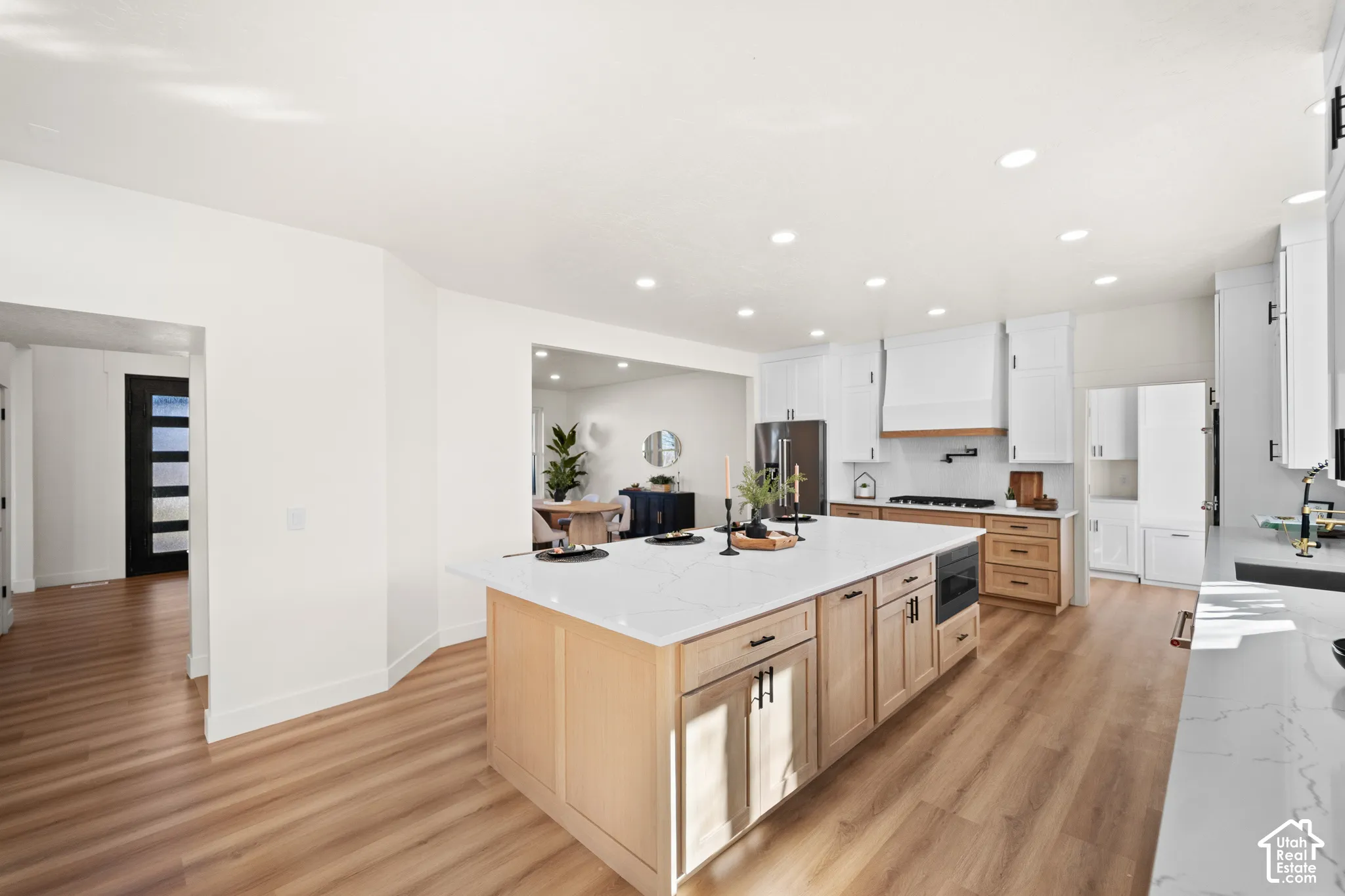 Modern kitchen featuring wood-finish flooring, a large island with a light-toned countertop, white cabinetry with black hardware, and a built-in microwave