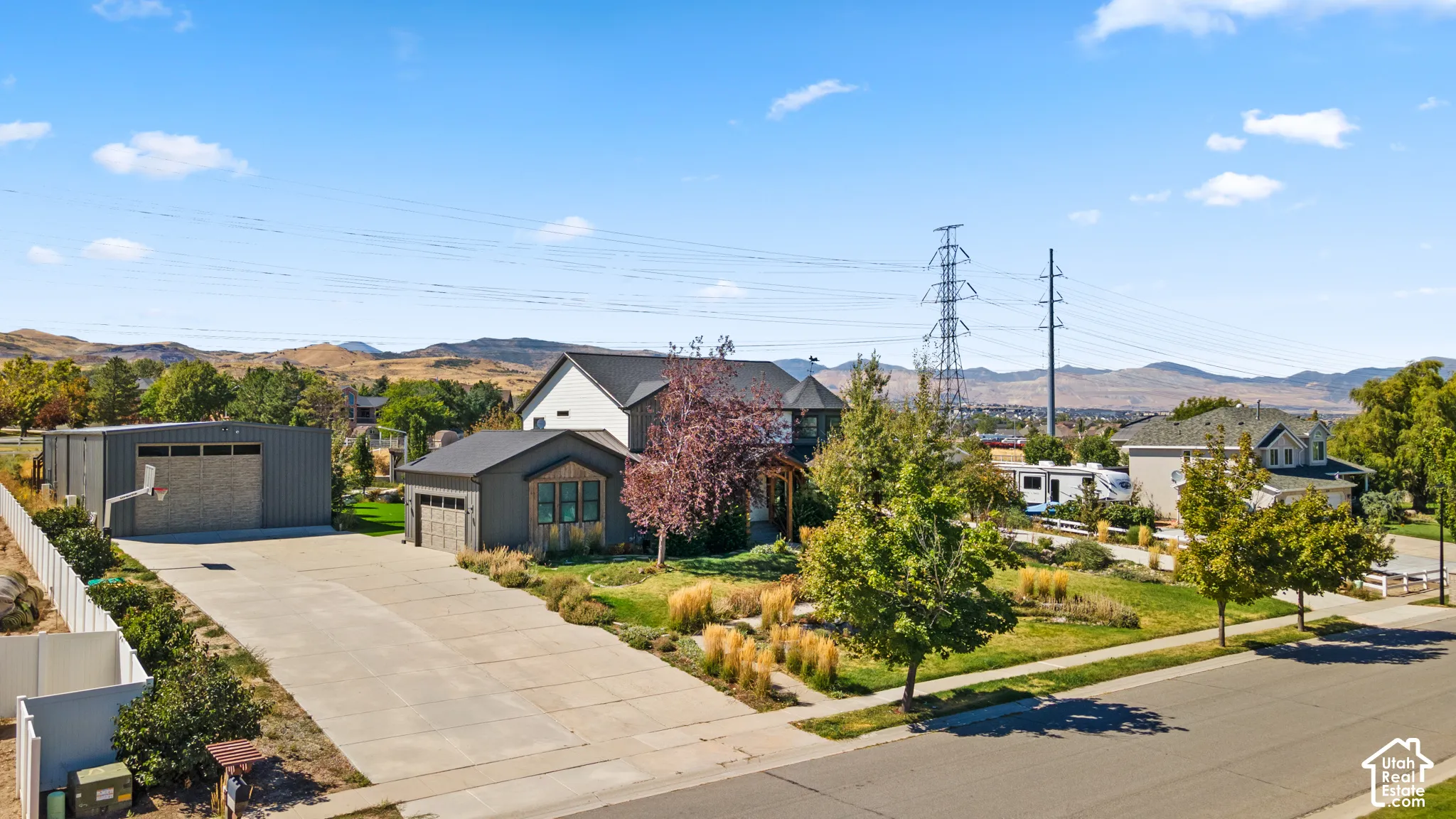 Expansive concrete driveway, detached garage with wood-finish doors, additional workshop structure, and mature landscaping