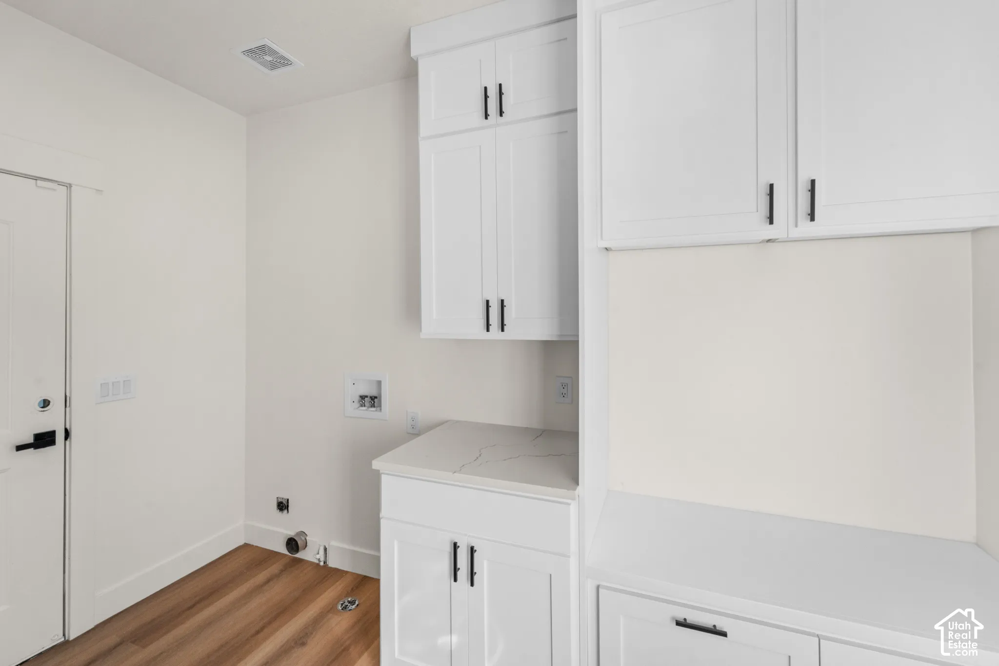 White shaker cabinetry with black hardware, wood-finish flooring, and a stone-finish countertop