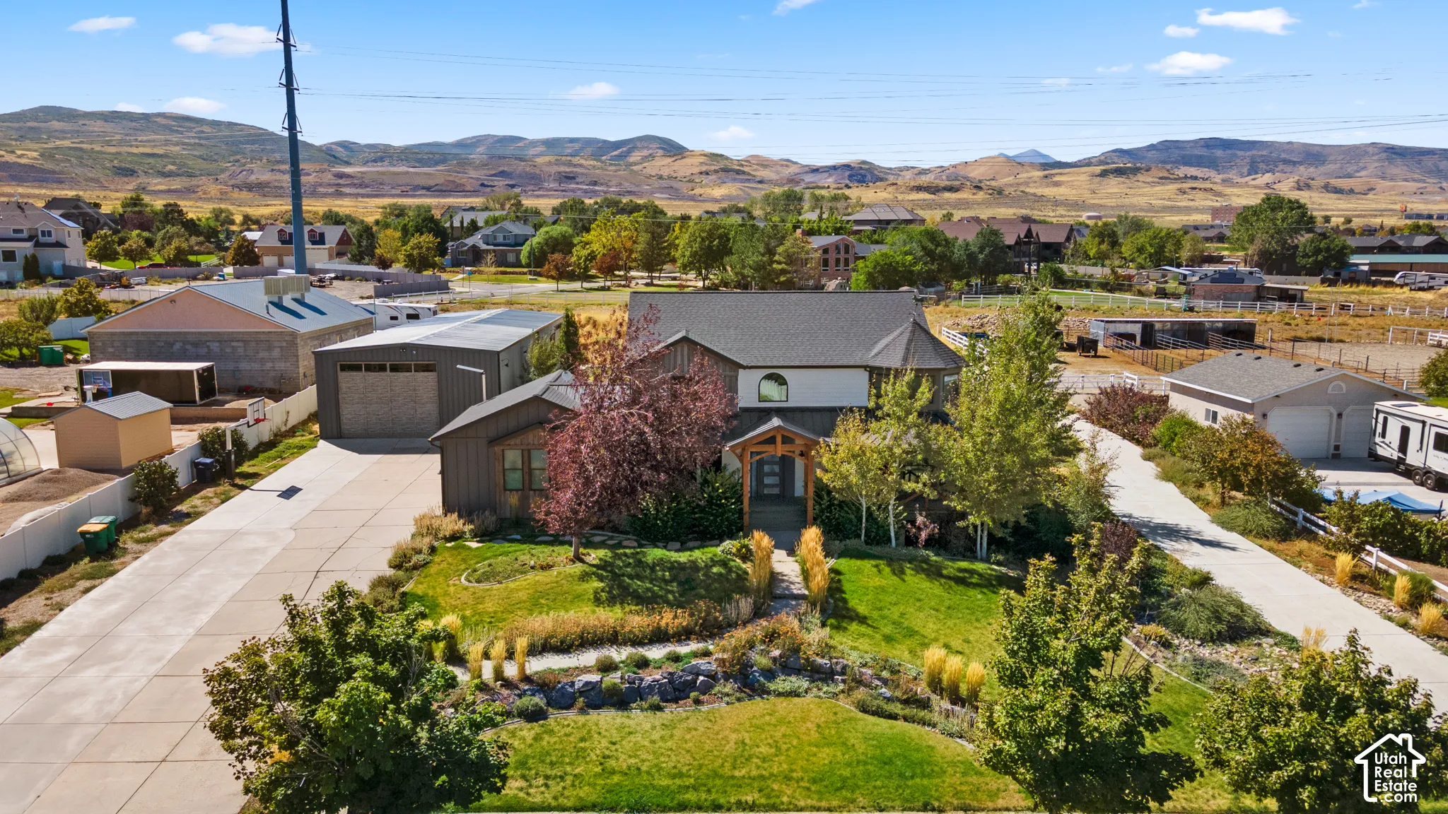Property featuring a multi-level exterior, an attached garage, a detached accessory building, a paved driveway, and mature landscaping