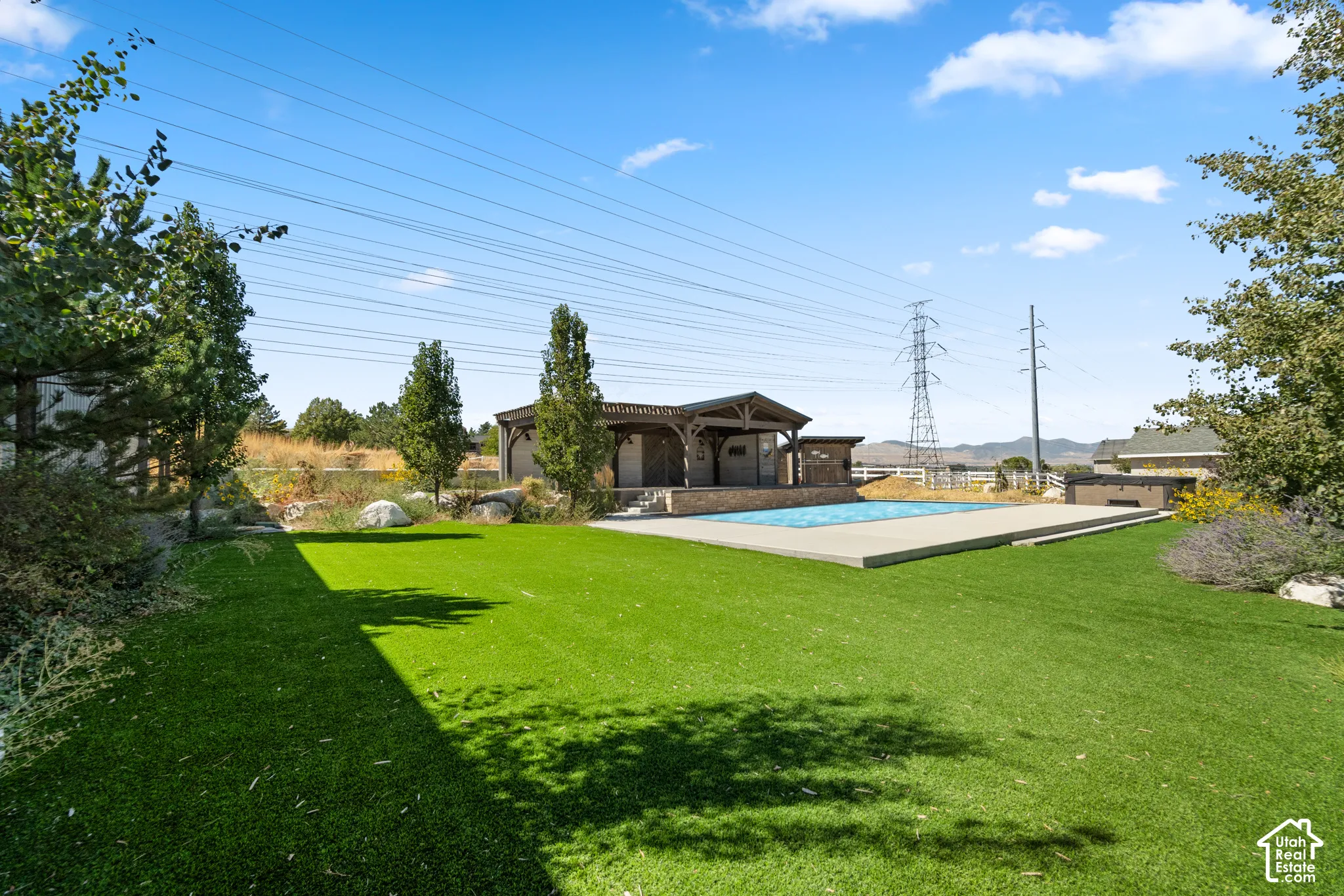 Expansive turf lawn with an in-ground swimming pool, stone-clad pool house, concrete pool decking, and mature landscaping