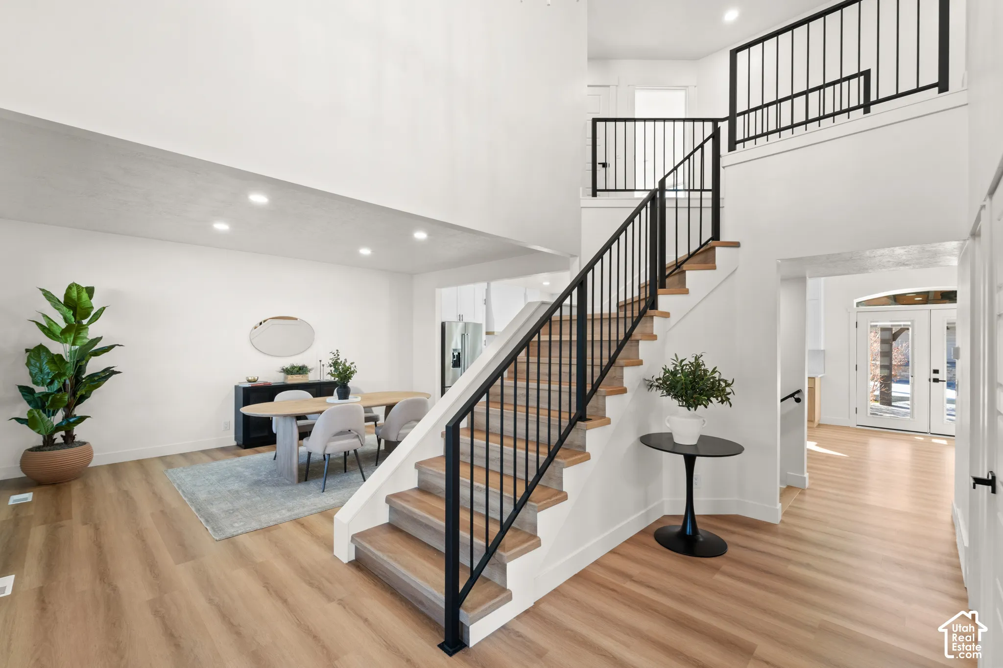 High ceilings, wood-finish flooring, recessed lighting, white walls, and black metal railings