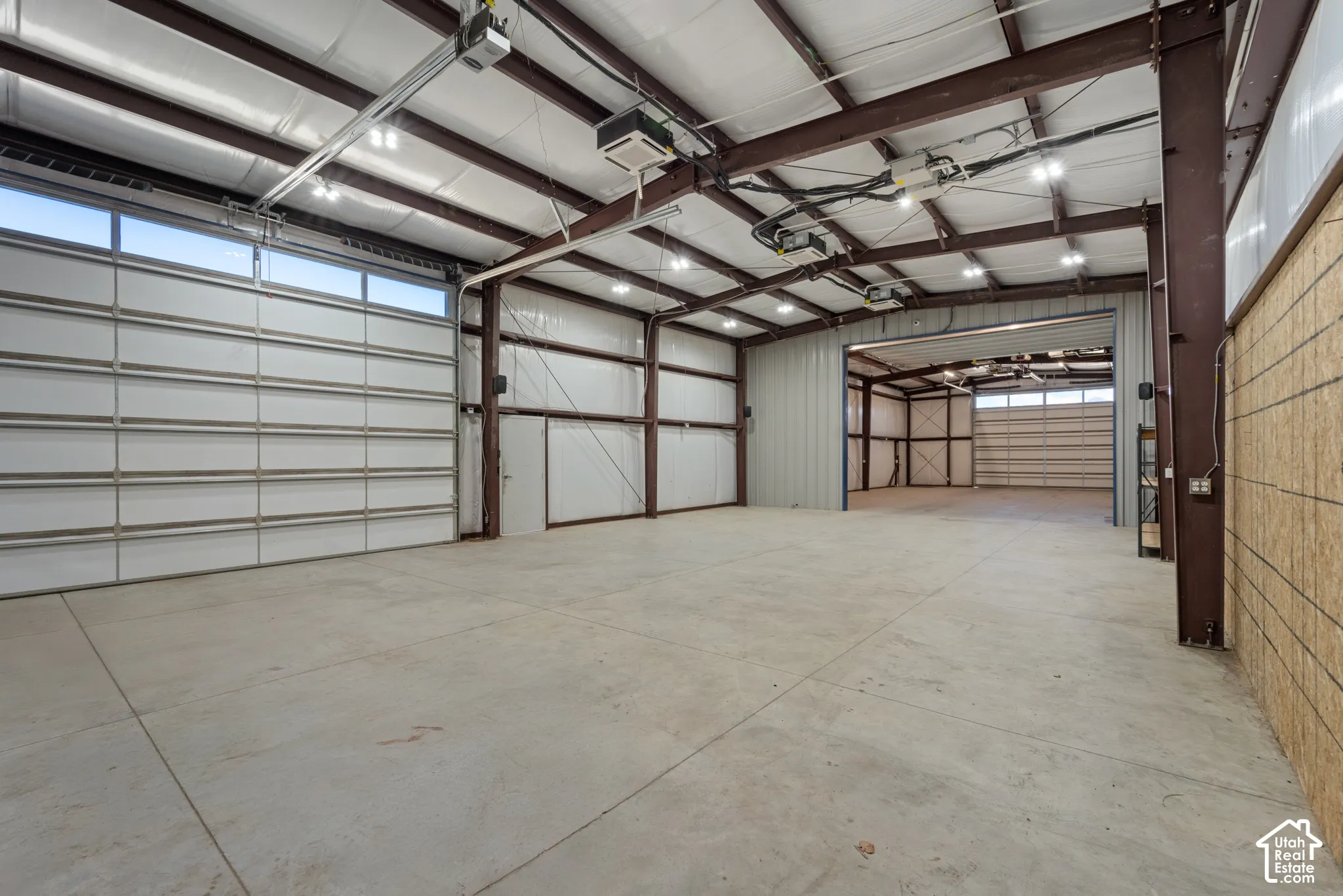Expansive concrete flooring with high ceilings, multiple overhead garage doors, and exposed structural beams