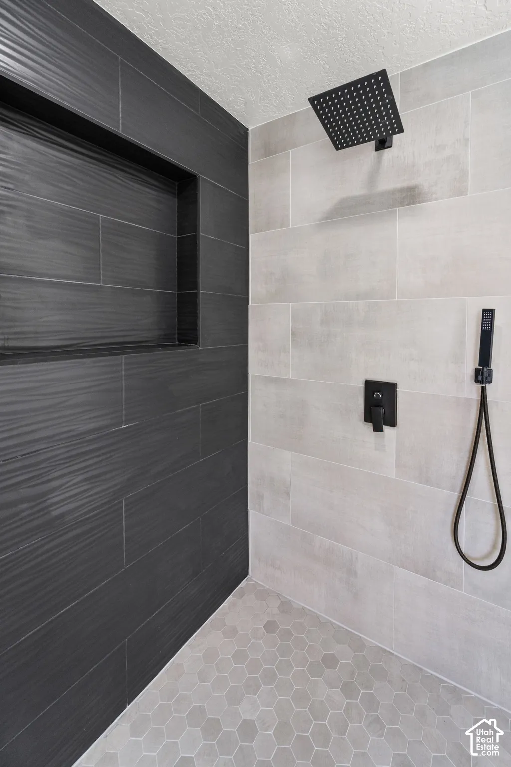 Shower featuring a built-in niche, matte black shower fixtures, light gray hexagonal floor tiles, and large format wall tiles in contrasting tones