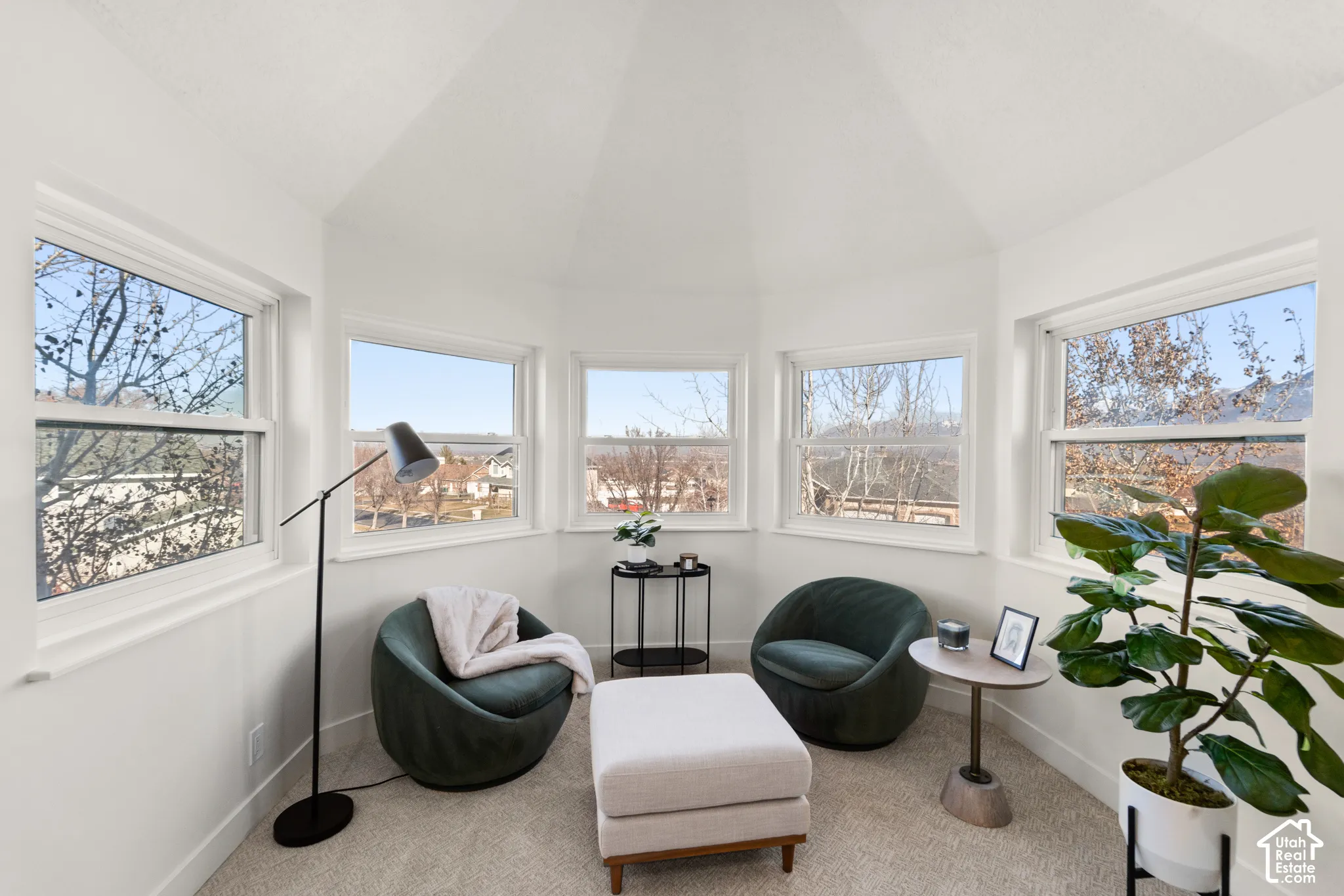 Angled room with multiple large windows, white walls, and light-colored carpeting