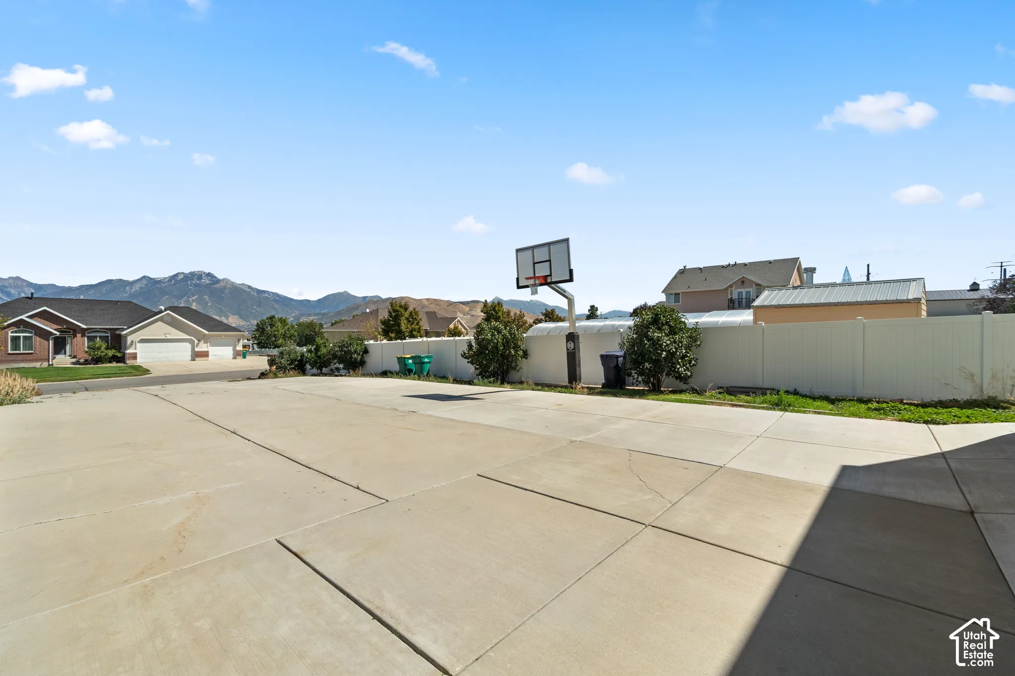 Expansive concrete pad, white privacy fencing, and a permanent basketball hoop
