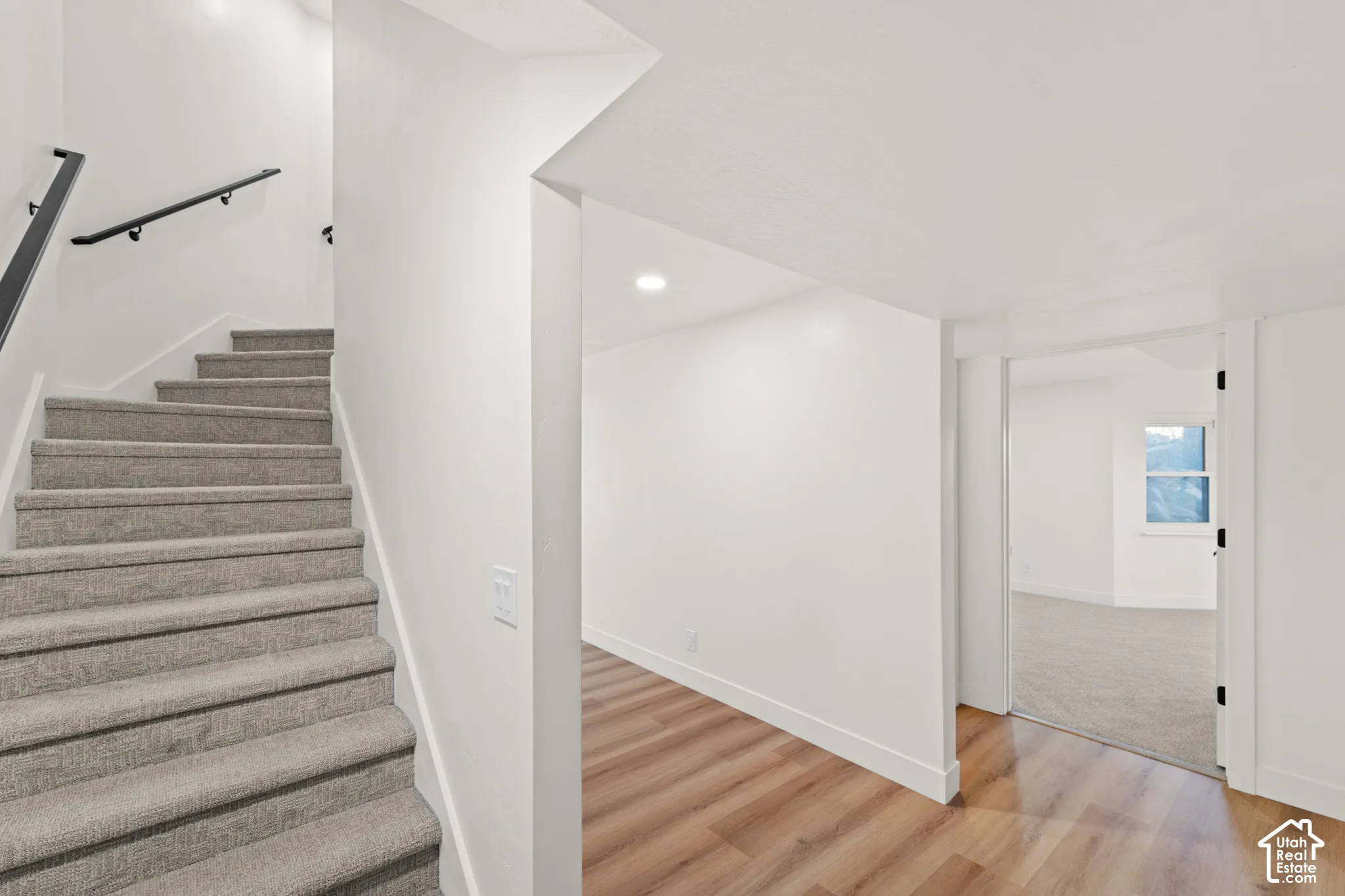 Carpeted staircase with black handrails, wood-finish flooring, and recessed ceiling lighting