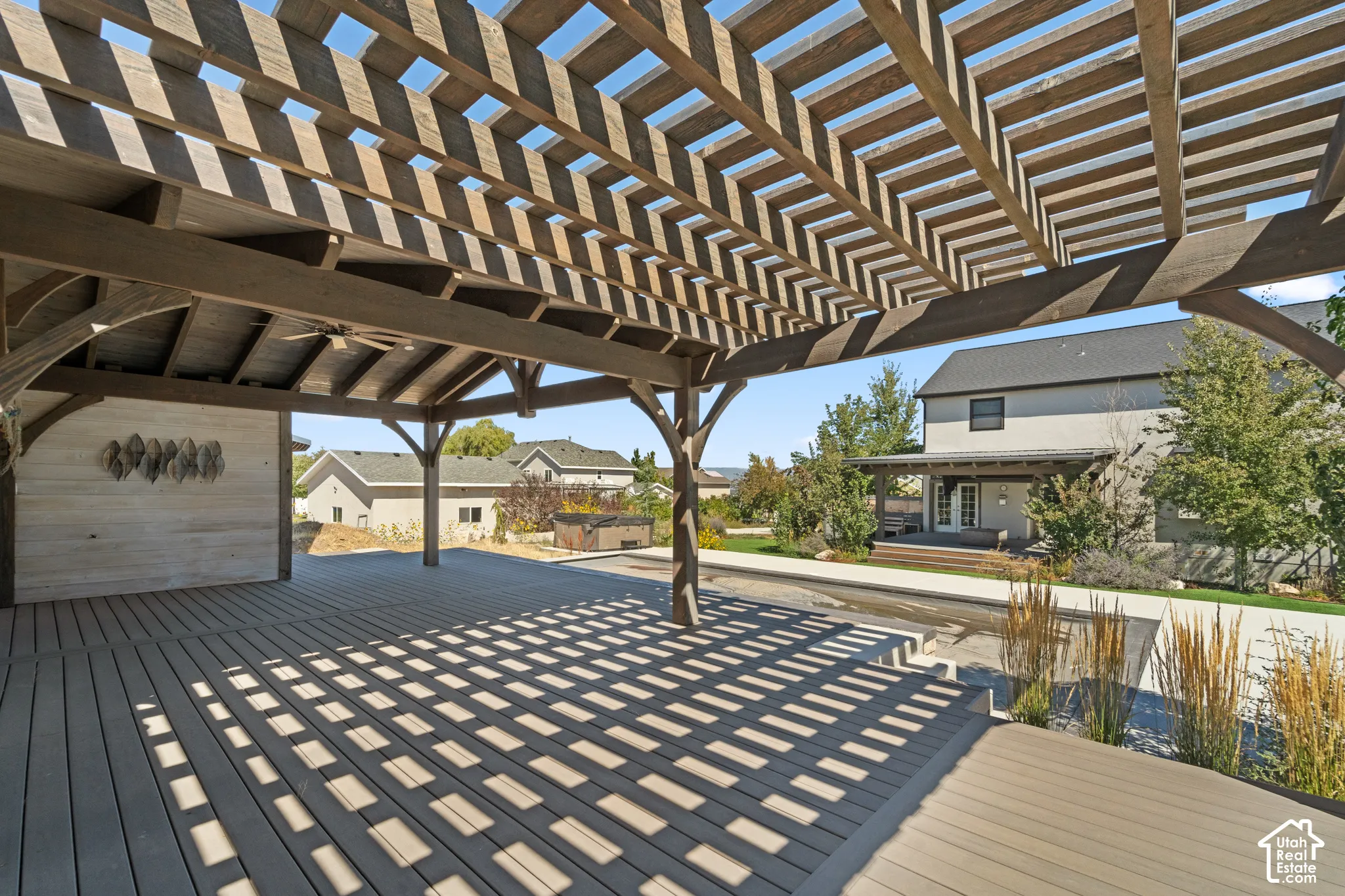 Expansive outdoor decking with a large pergola structure, featuring a built-in ceiling fan and an integrated accent wall