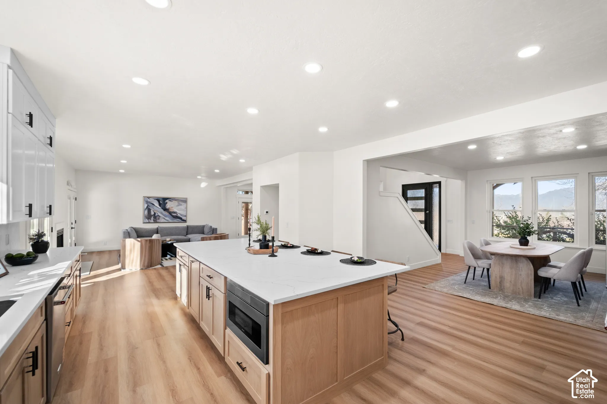 Open-concept living area with wood-finish flooring, recessed lighting, a kitchen island with integrated microwave, and white cabinetry with dark hardware