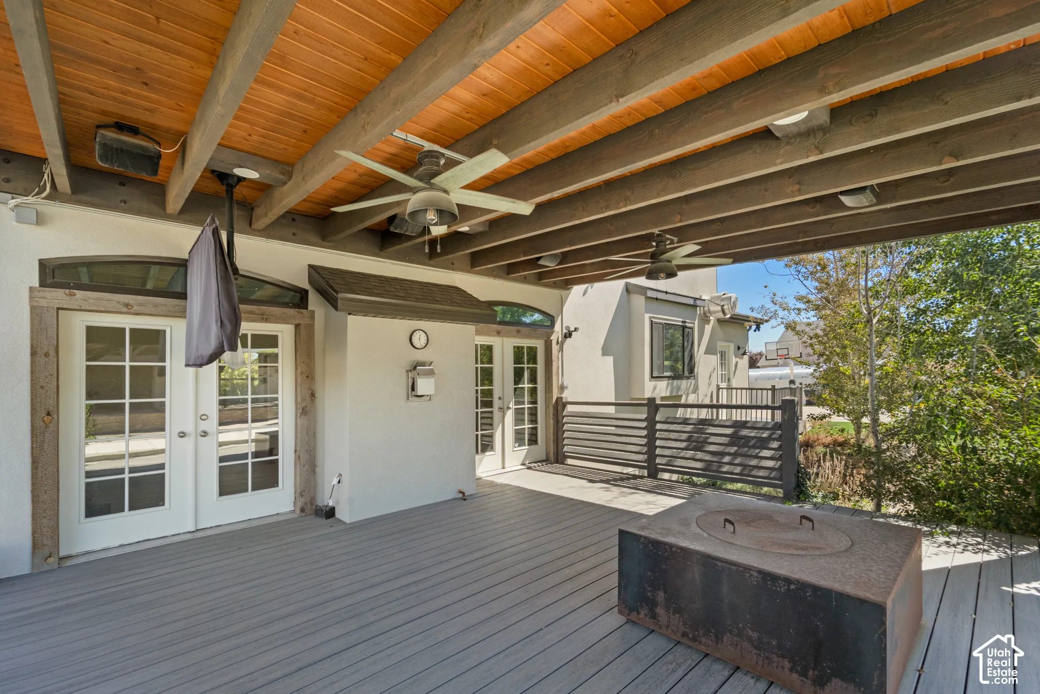 Expansive outdoor deck featuring wood-finish ceiling, exposed beams, multiple ceiling fans, and a built-in fire pit