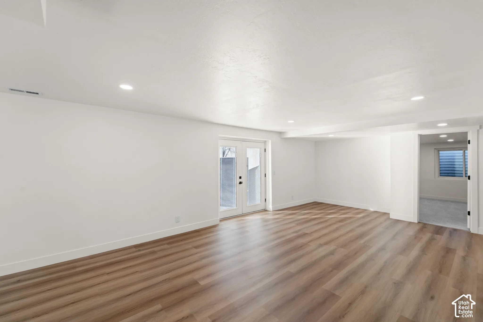 Spacious room featuring wood-finish flooring, white walls, recessed lighting, and white French doors