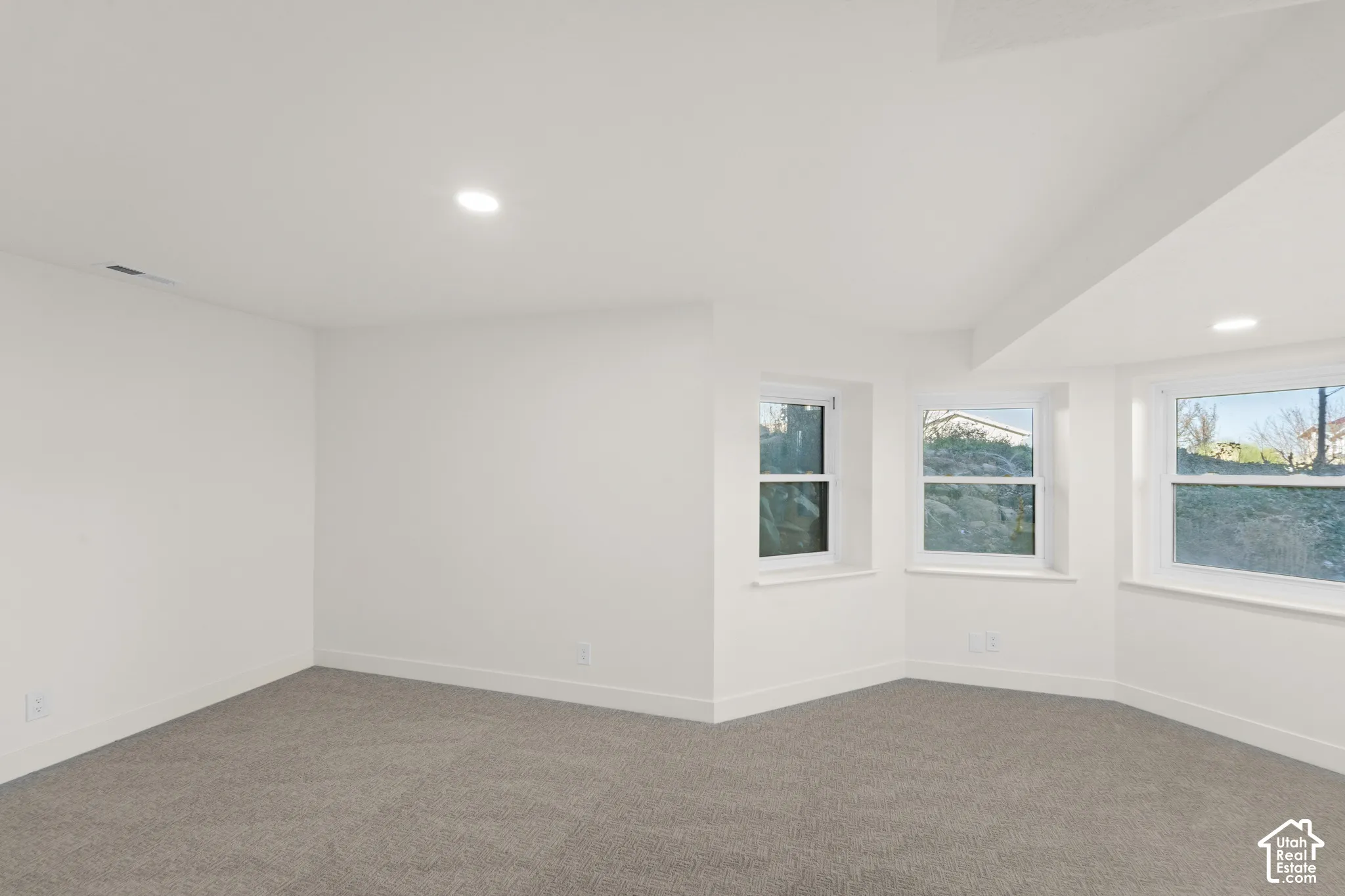 Recessed lighting, white walls, gray carpeting, and multiple windows with white trim