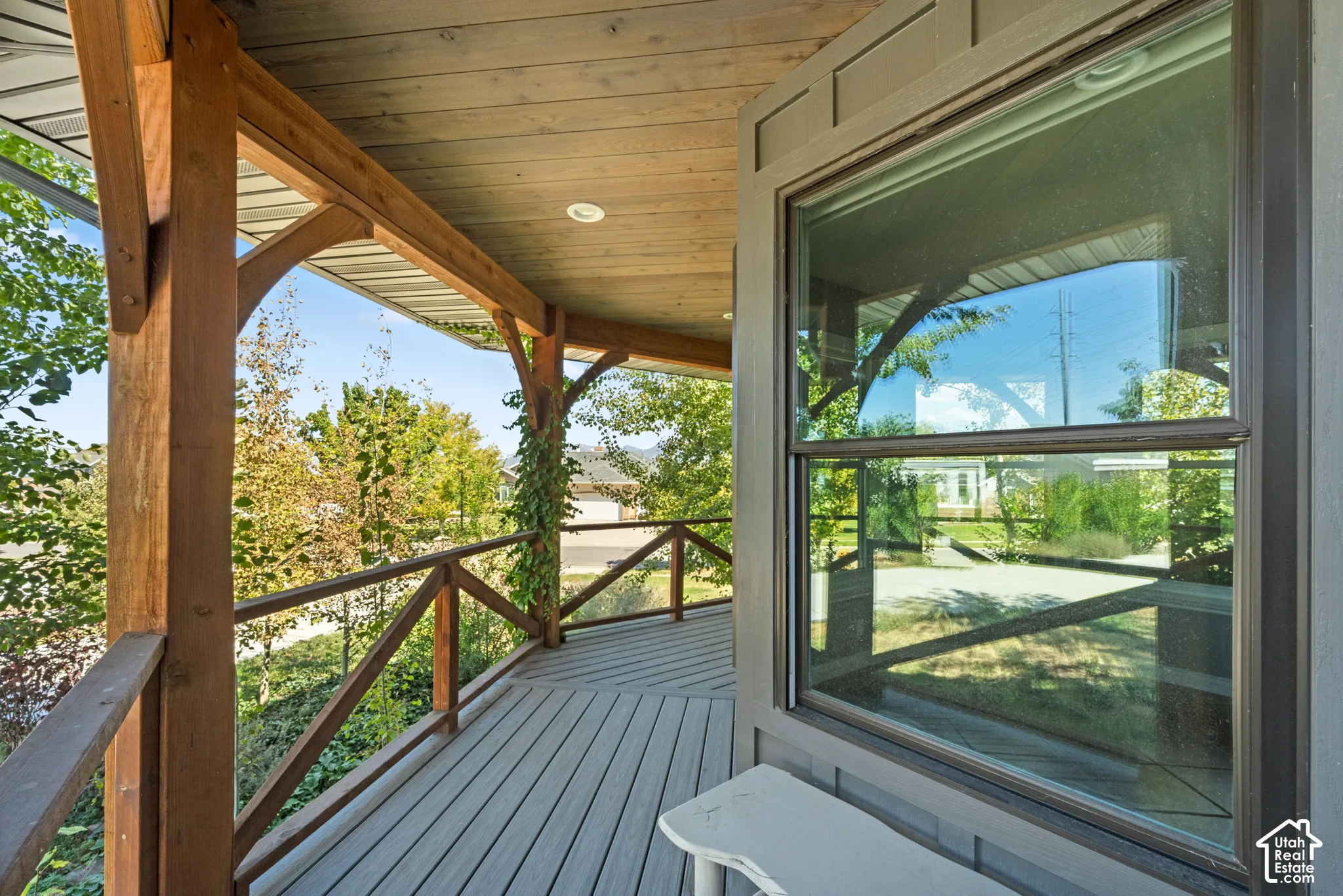 Covered exterior porch featuring wood beams and railing, plank decking, and a large window with trim