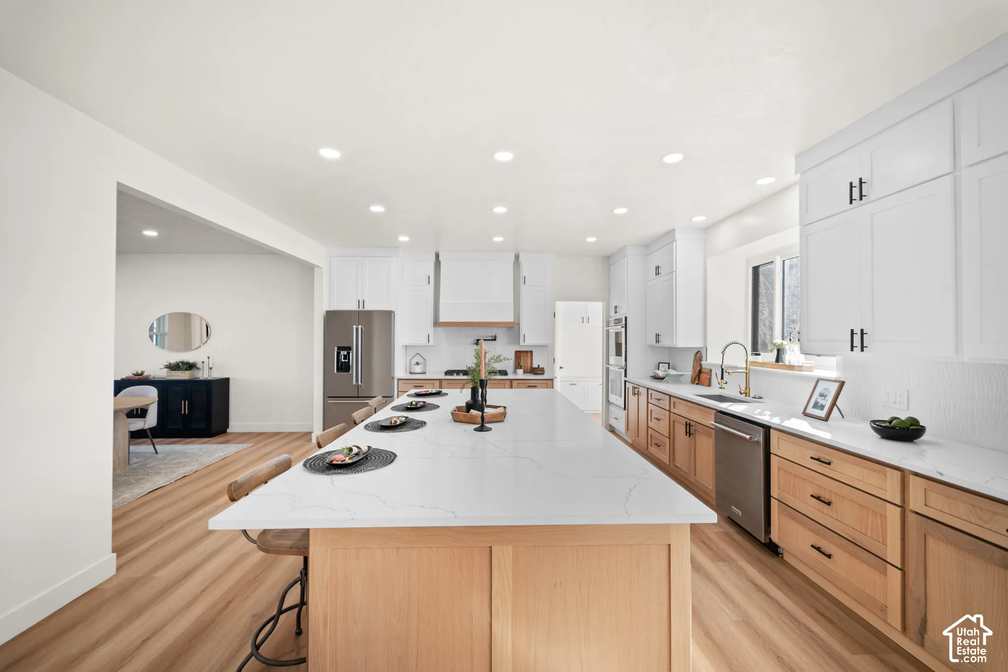Spacious kitchen featuring an expansive central island with a light-toned countertop, wood-finish flooring, white upper cabinetry, and natural wood-tone lower cabinetry