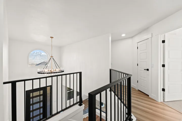 Arched window with mountain scenery, contemporary chandelier, black metal railings, wood-finish flooring, and white paneled doors
