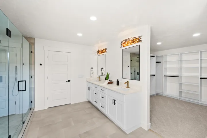 Spacious bathroom featuring a dual vanity with white cabinetry, gold-finish fixtures, and a glass-enclosed shower