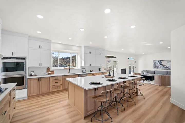 Open-concept kitchen featuring an expansive island with seating, stainless steel appliances, two-tone cabinetry, and wood-finish flooring