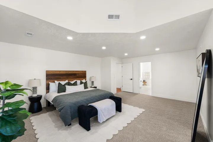 Vaulted ceiling with recessed lighting, wood-finish headboard, and light-toned carpeting