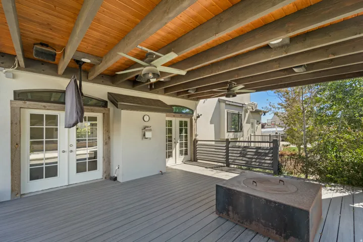 Expansive outdoor deck featuring wood-finish ceiling, exposed beams, multiple ceiling fans, and a built-in fire pit