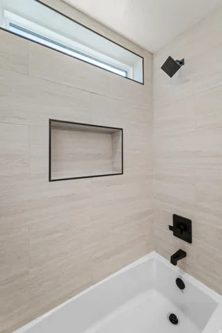 Built-in bathtub with matte black fixtures, full-height tiled surround, recessed wall niche, and transom window